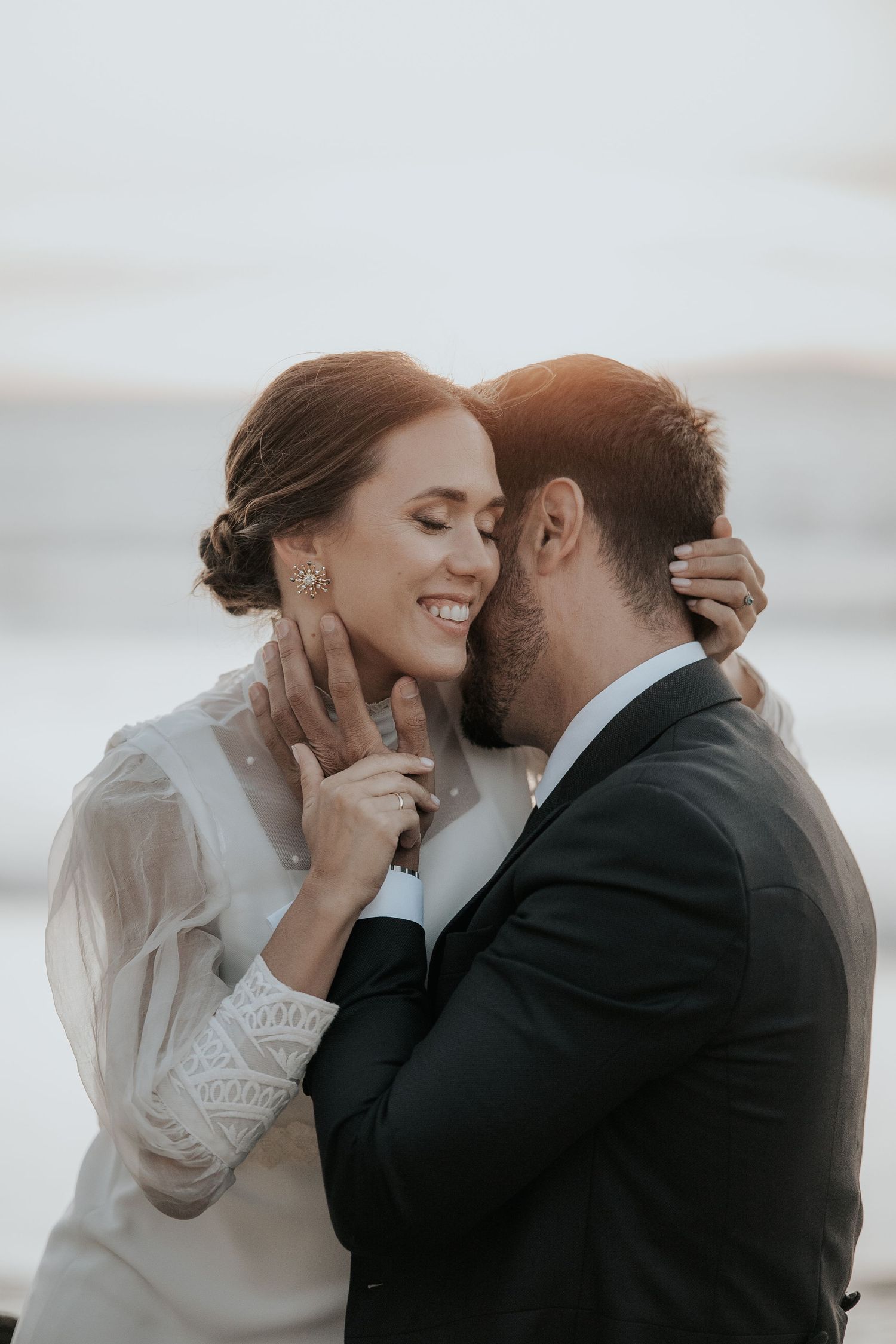Wedding couple embraces tenderly against a bright, ethereal background during sunset.