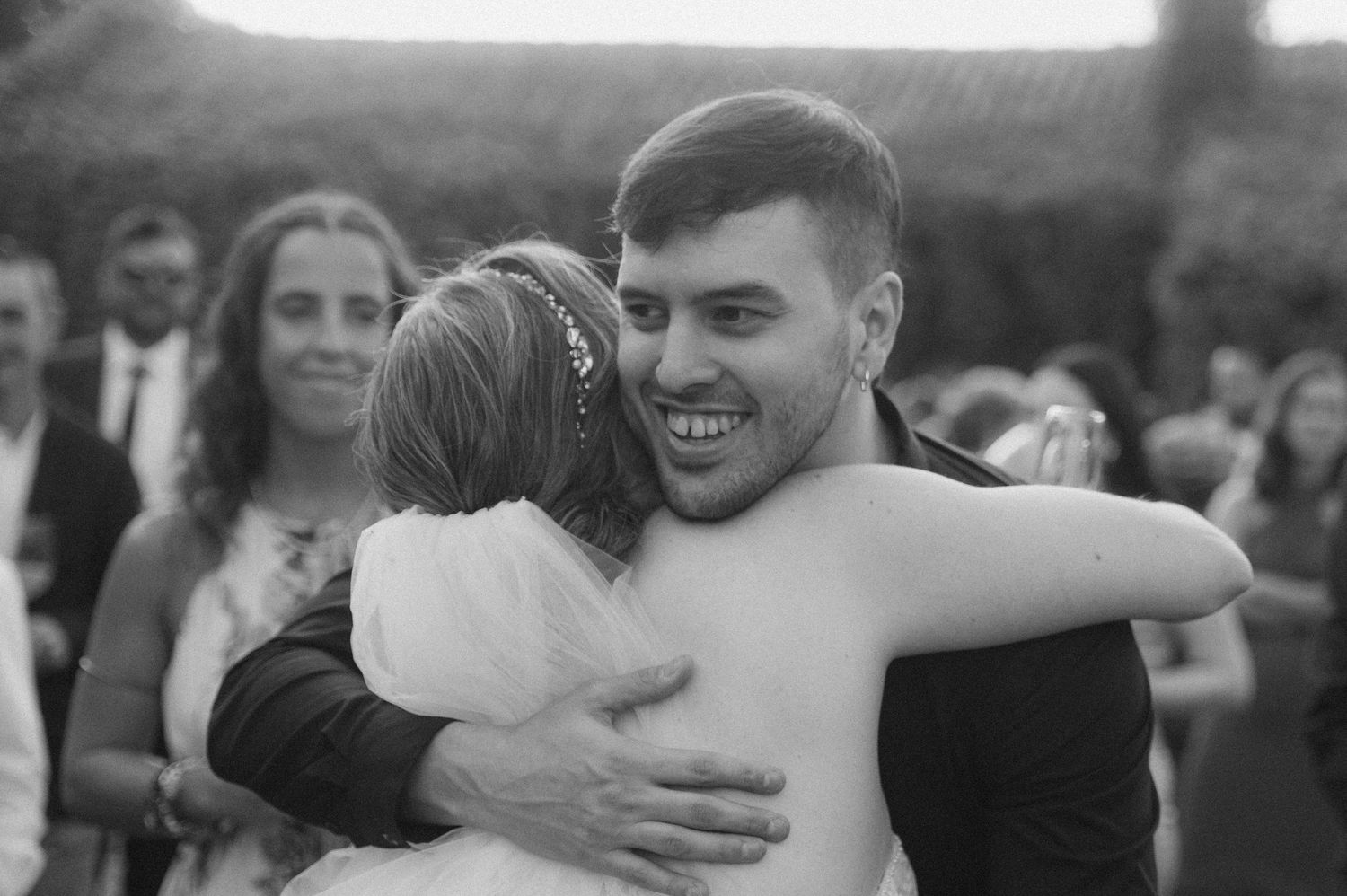 Black and white photo of wedding guests embracing during an outdoor celebration.