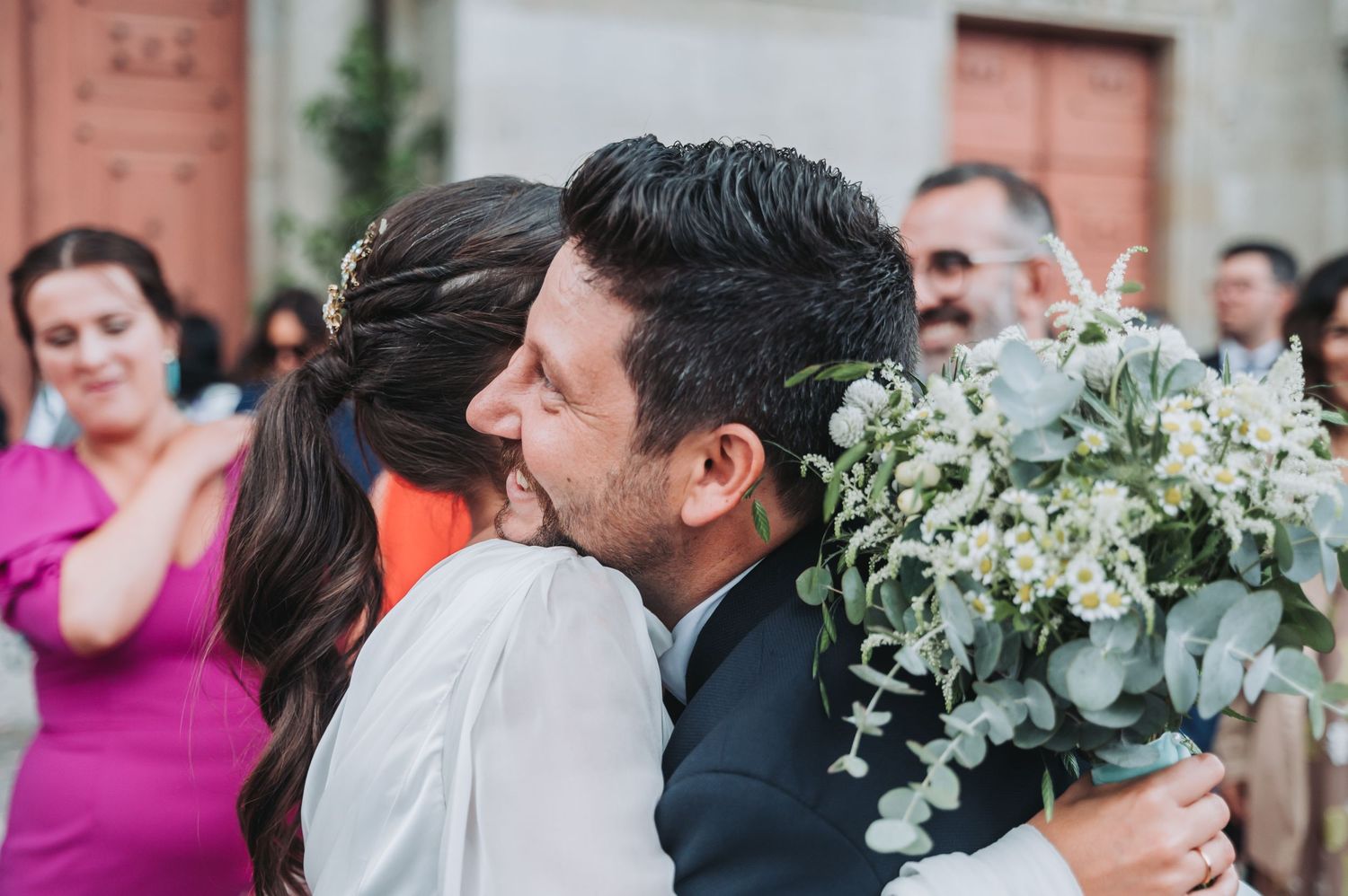 Wedding guests gather outdoors at a celebration surrounded by elegant greenery and floral decorations.