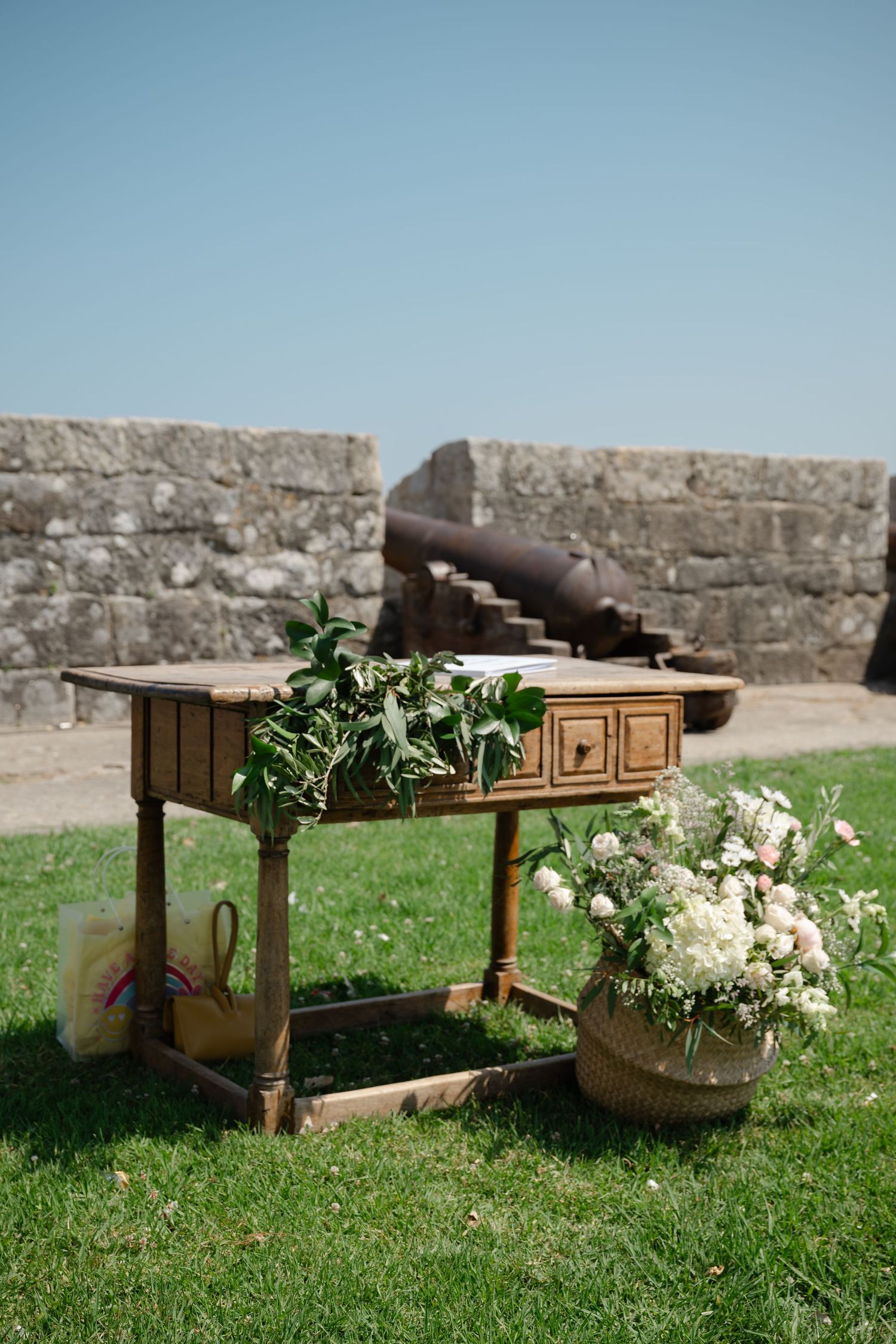 Wooden benches with white floral arrangements sit on grass against a stone wall backdrop.