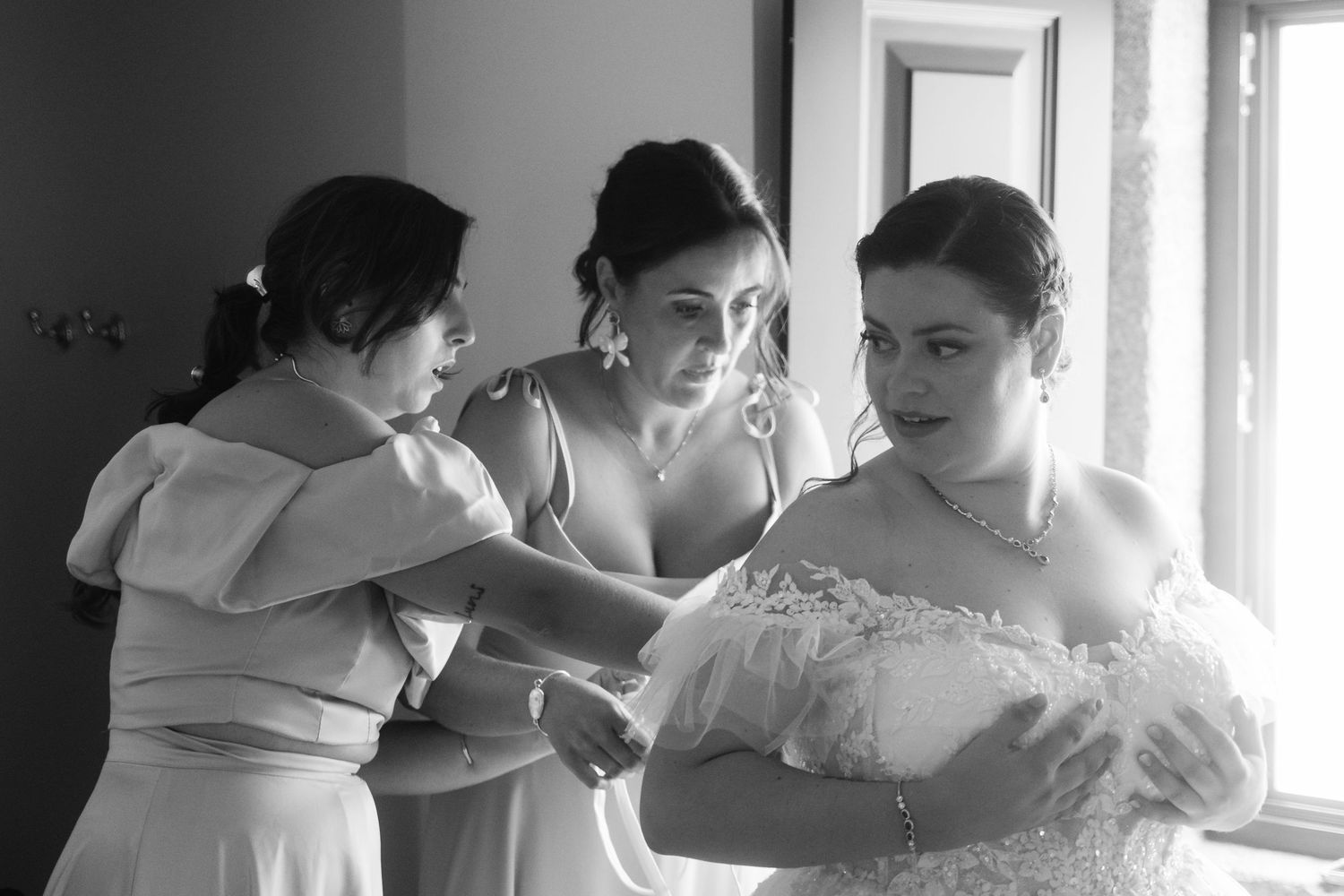 Black and white photo of people hugging and embracing in an emotional group moment by a window.