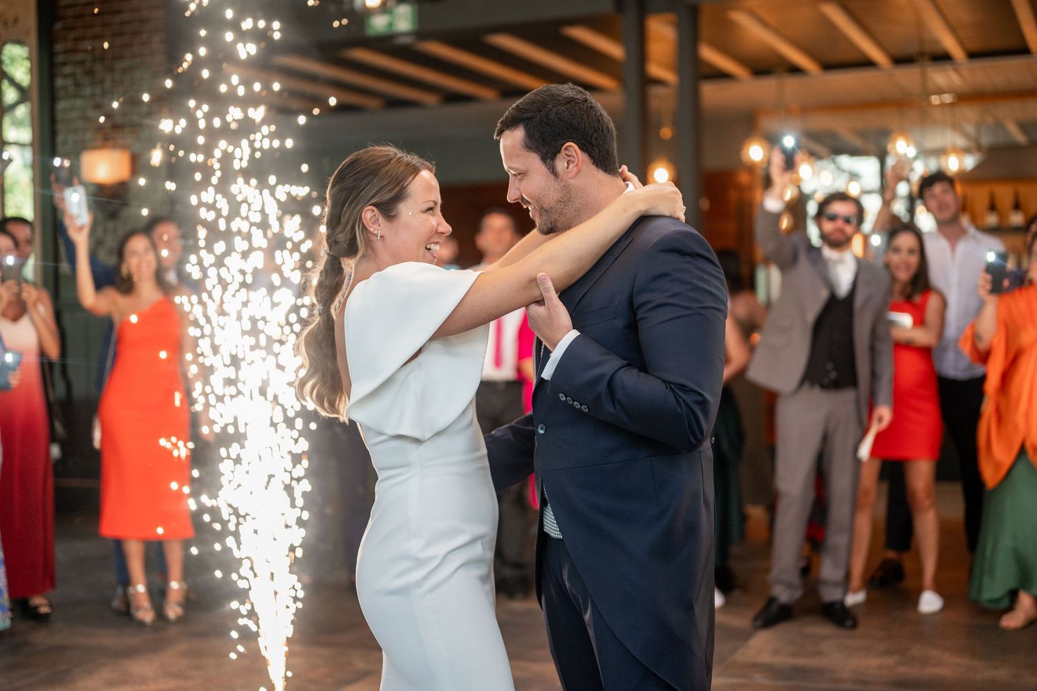 Wedding couple shares their first dance under twinkling lights at a rustic barn reception venue.