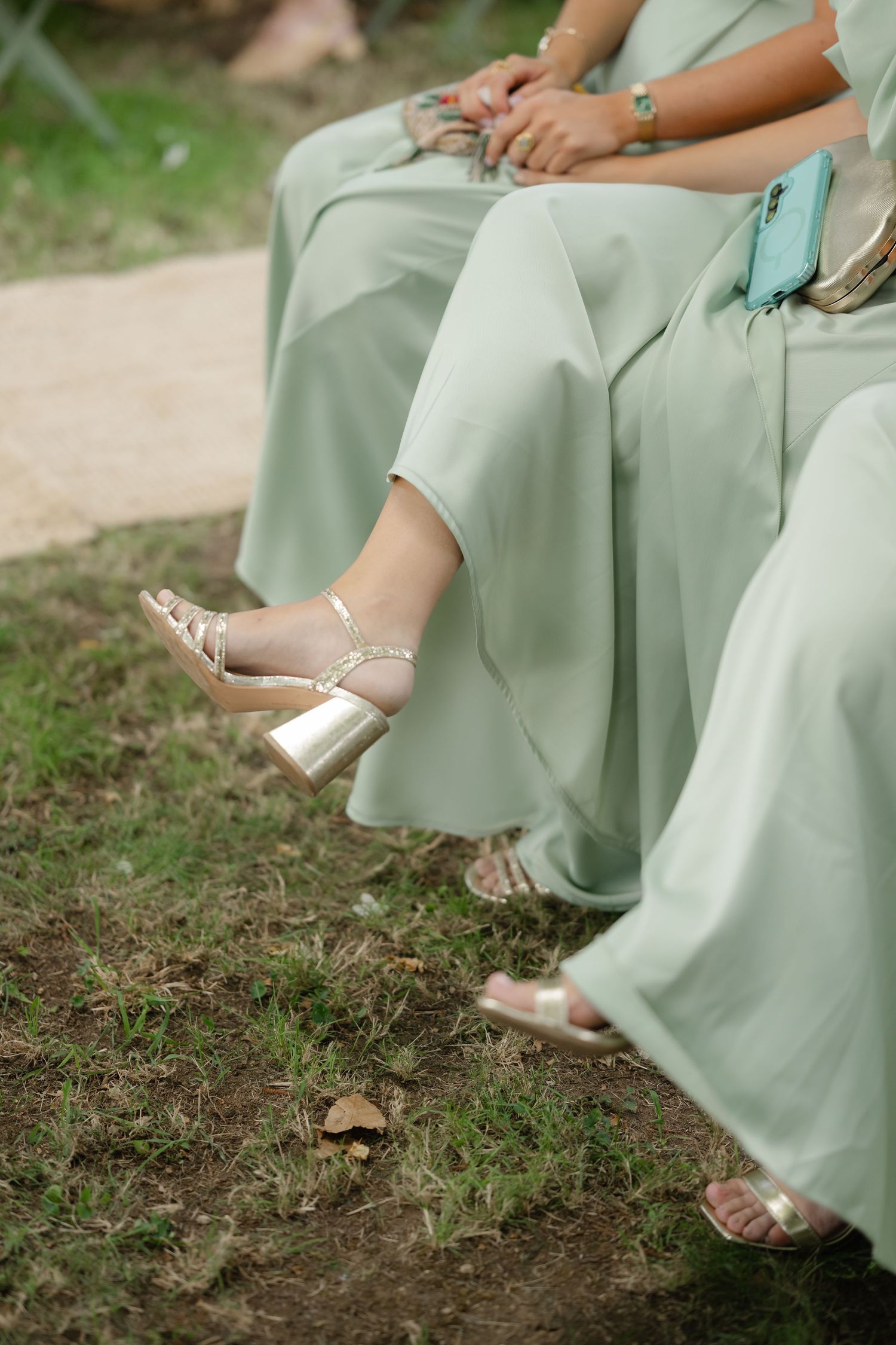 Close-up shots of mint green bridesmaid dresses and metallic sandals on grassy ground during an outdoor event.