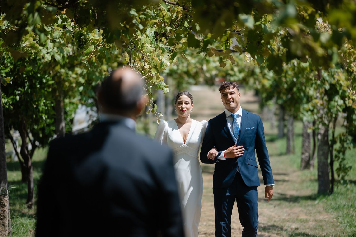 Wedding guests gather outdoors under green trees during an elegant garden ceremony celebration.