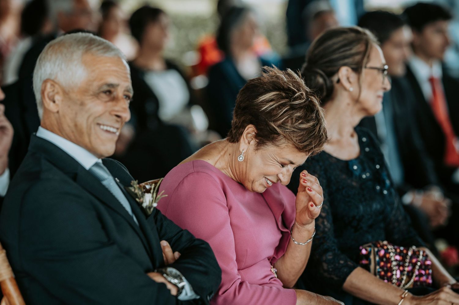 A group of people in formal attire laugh together during an event while seated in an audience.