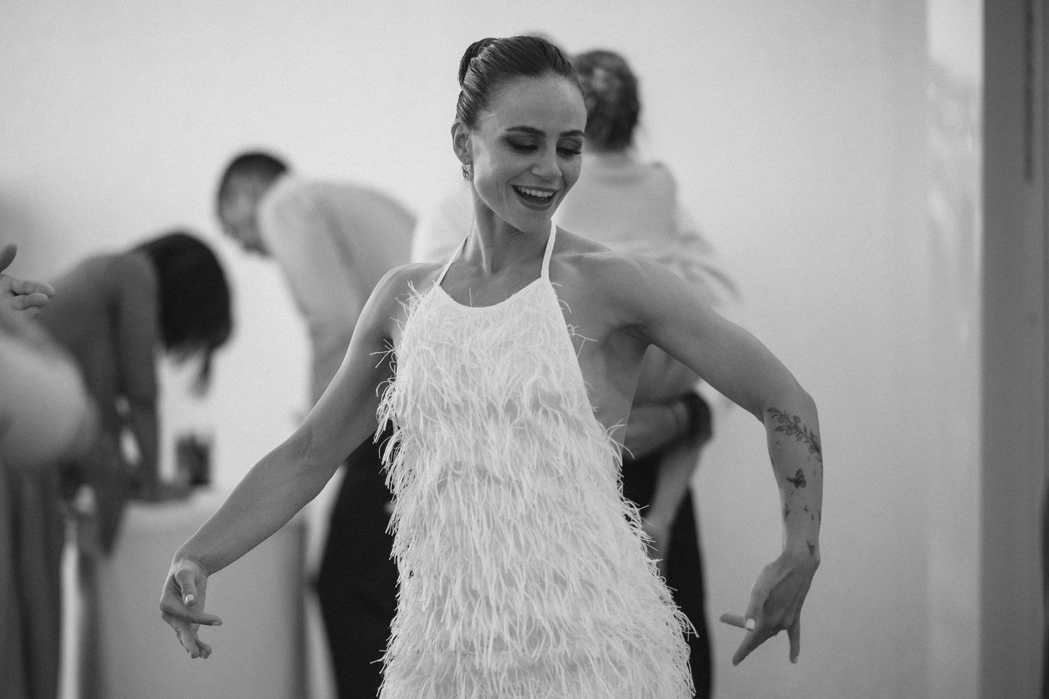 A bride in a feathered white dress twirls and dances during a wedding celebration.