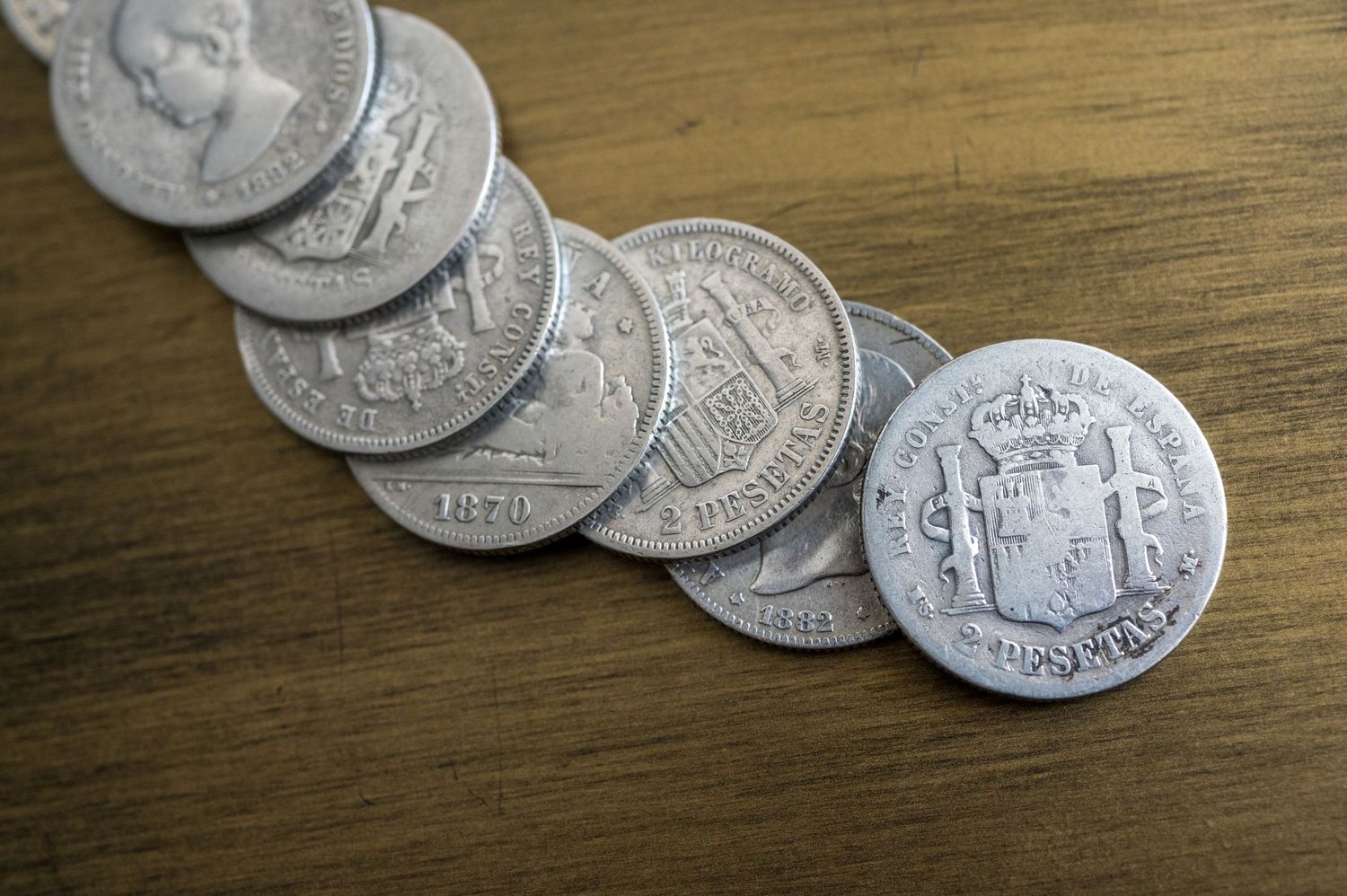 Vintage silver coins arranged in a curved line on a wooden surface.