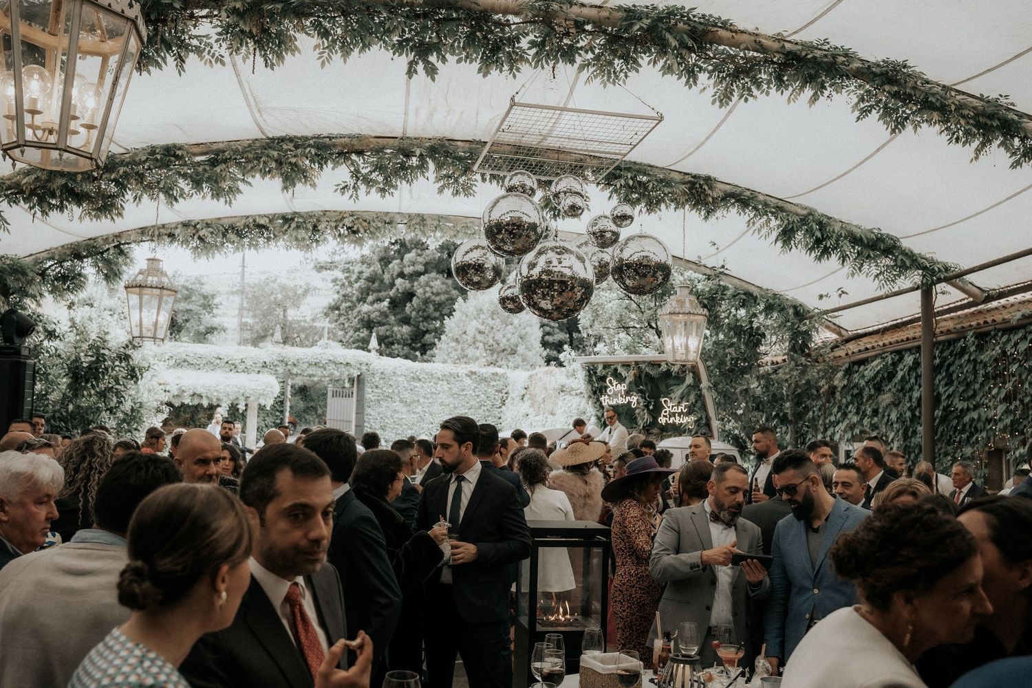 A wedding reception celebration under a clear tent decorated with lush greenery and twinkling lights.