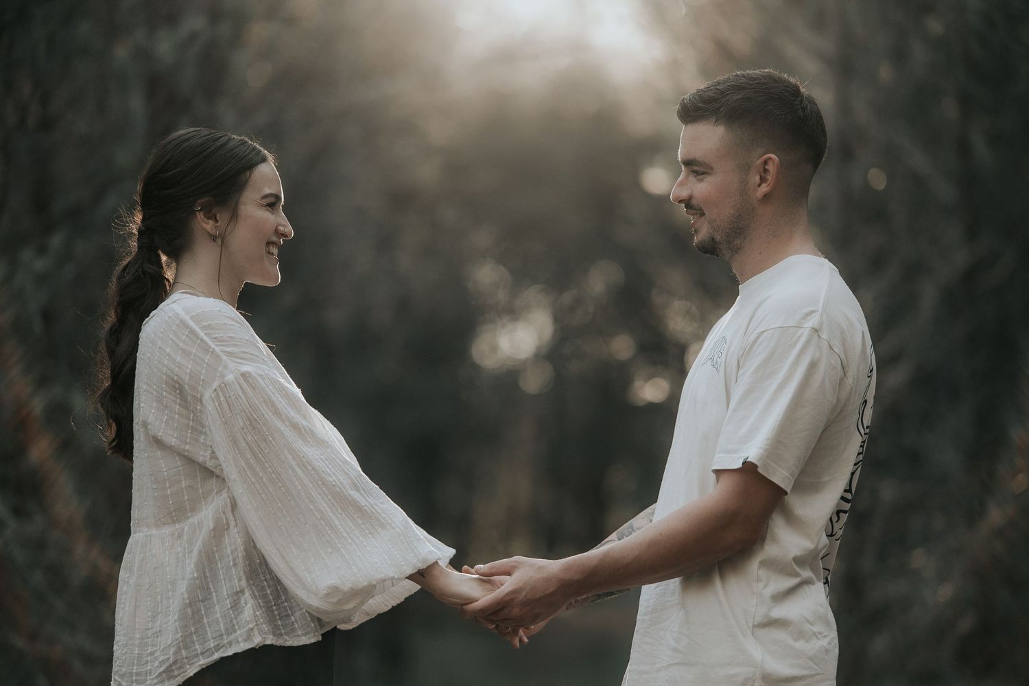 Romantic couple embracing in a moody forest setting with sunlight streaming through trees.