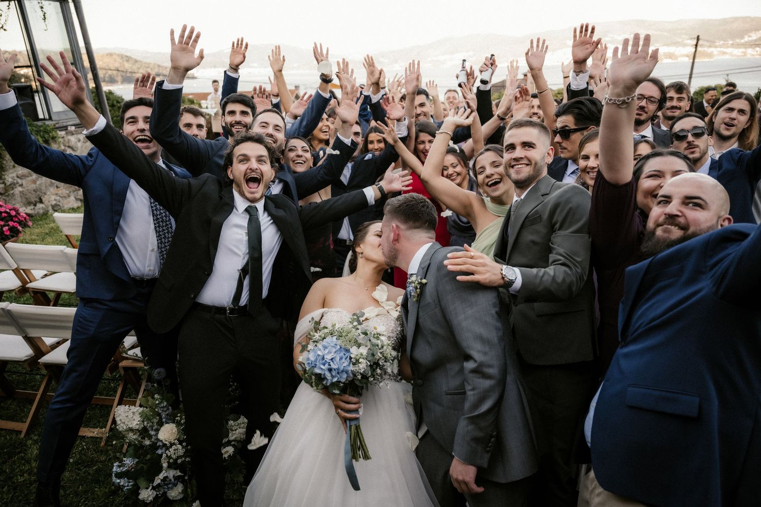 Wedding guests and couple raise their hands in celebration during outdoor reception.