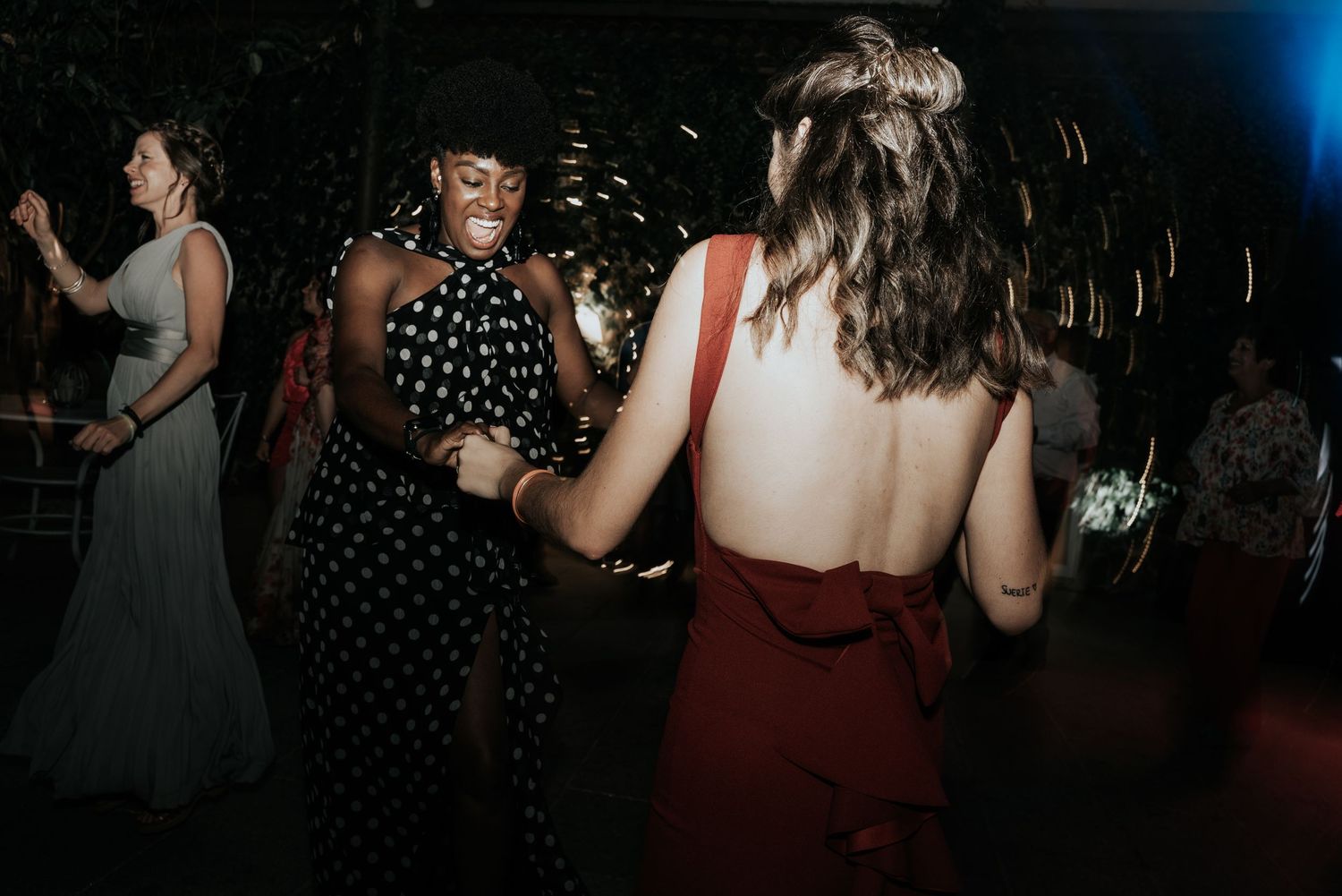 People dancing and celebrating at a dimly lit party or reception venue with festive lighting.