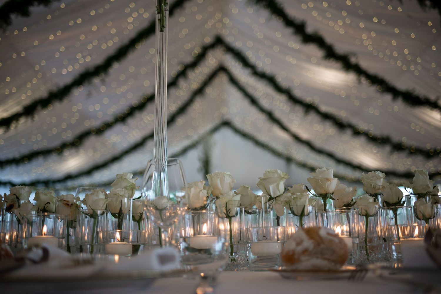 Elegant wedding reception table setting with glowing candlelit centerpieces under a draped ceiling with twinkling lights.