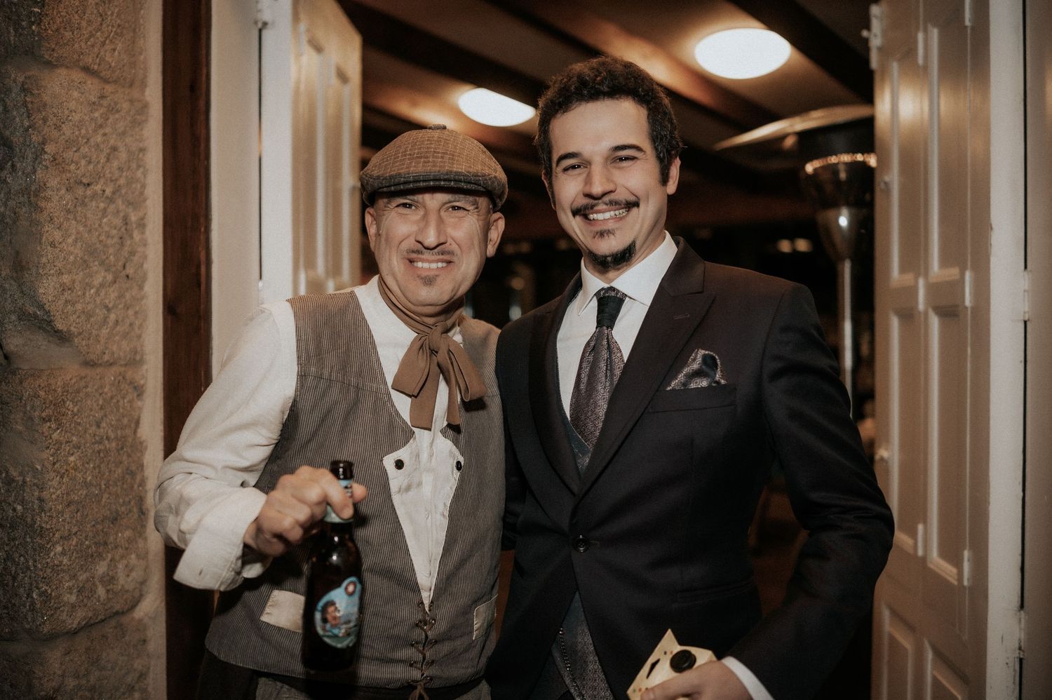 Two well-dressed guests pose together in a hallway during an evening celebration.