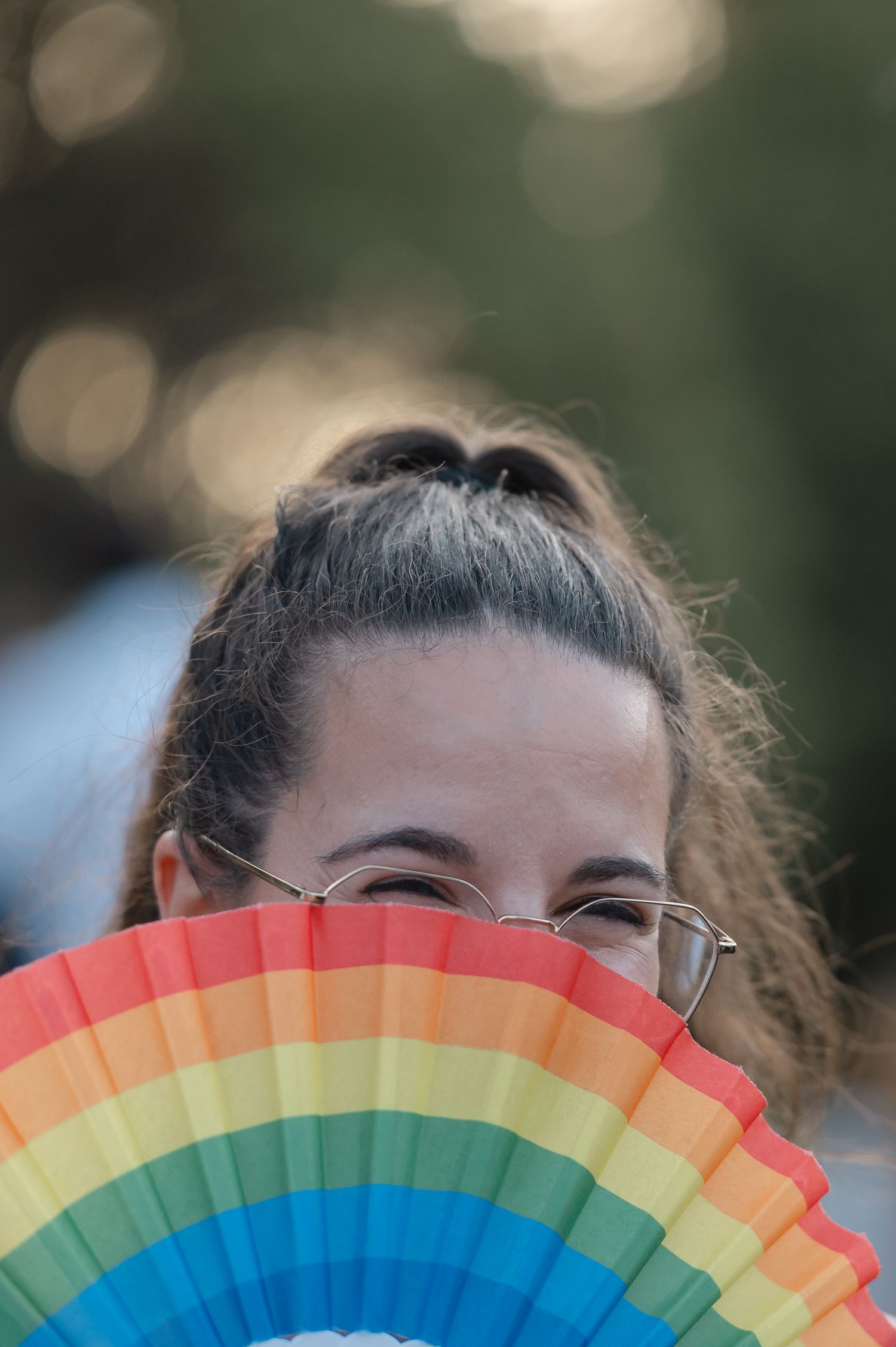 Person holding up a colorful rainbow-patterned folding fan against a blurred green background.