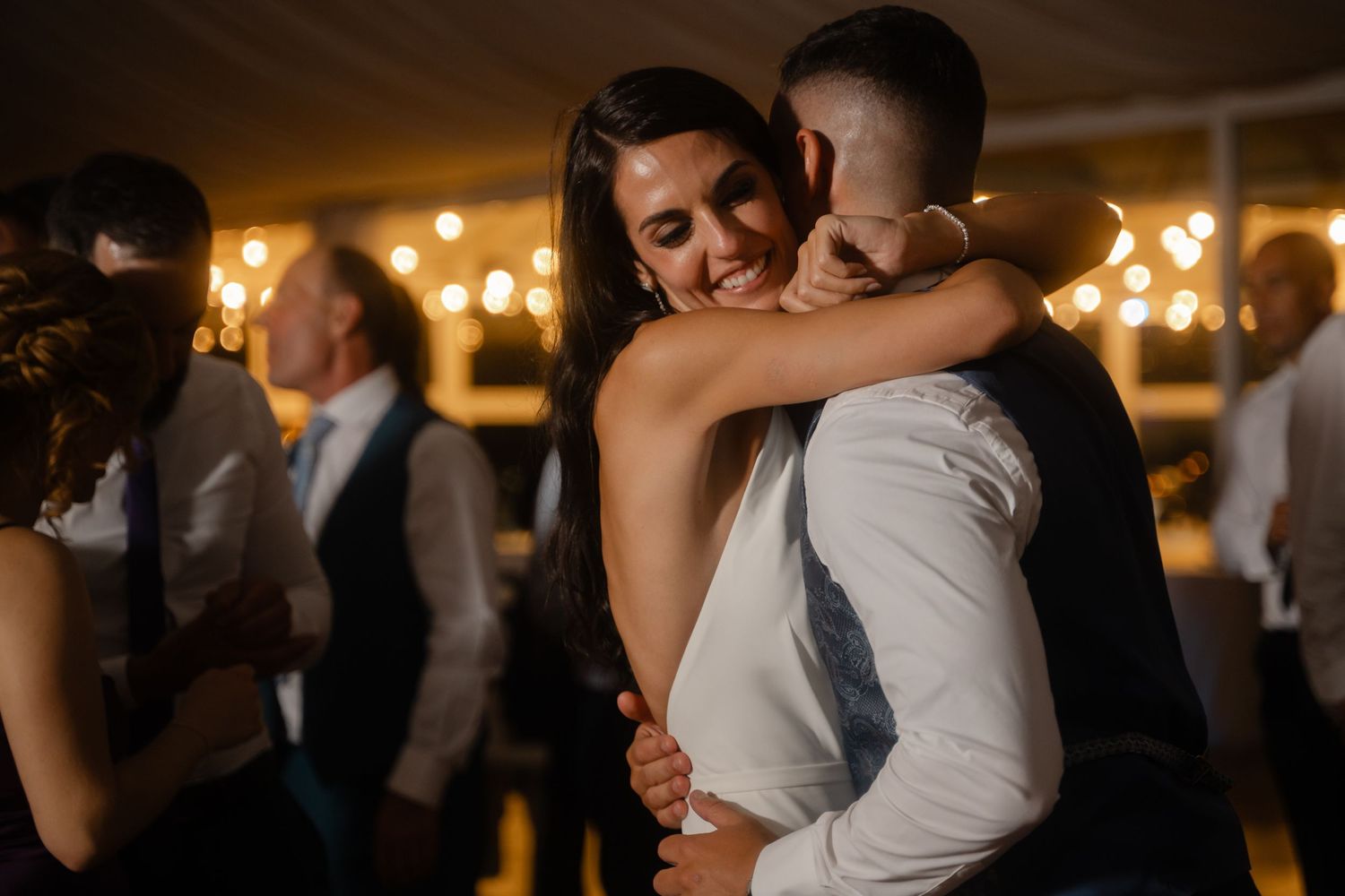 Couples dancing together at an elegant evening wedding reception with warm lighting in the background.