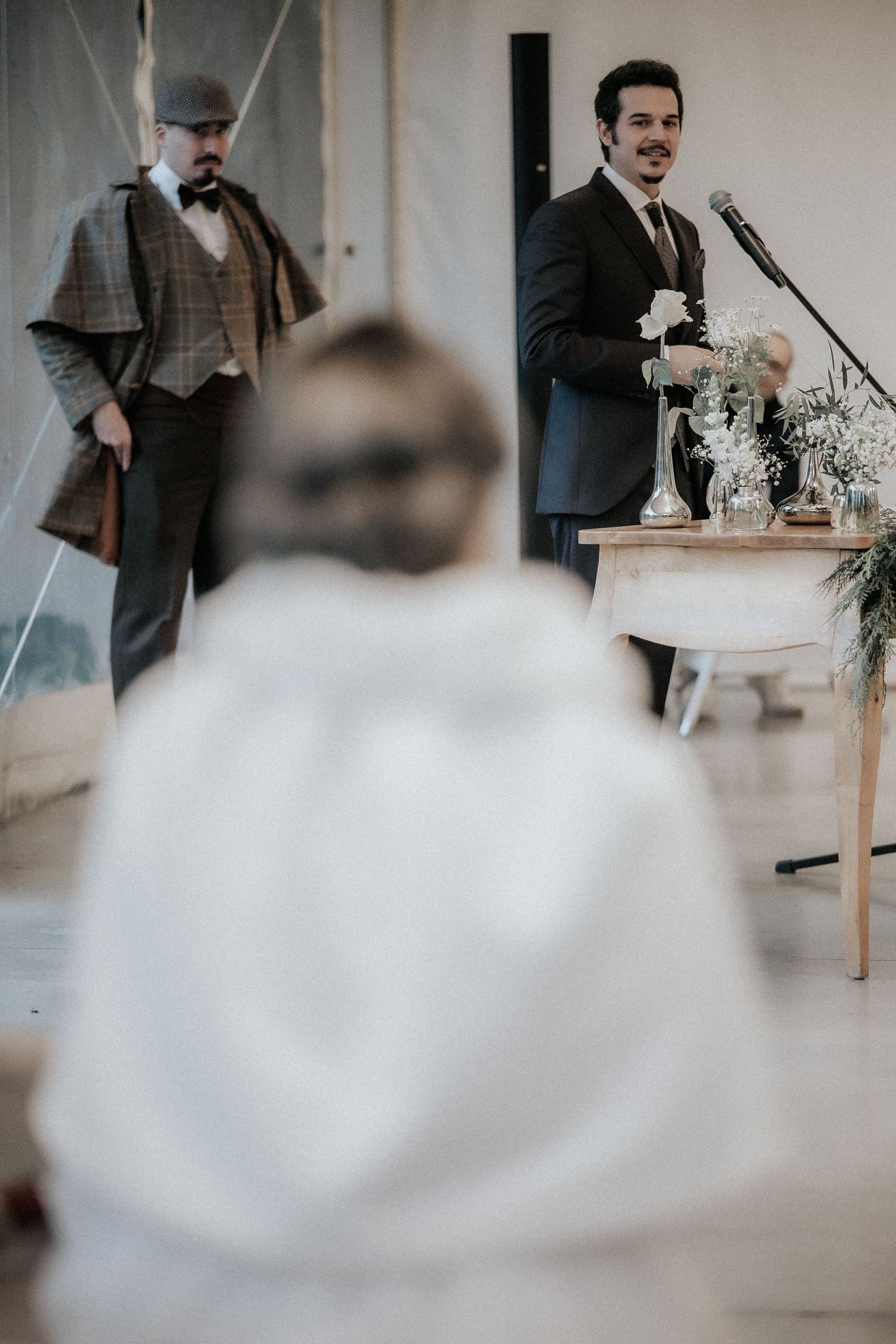 A wedding reception scene with elegant decor and guests seated at tables indoors.