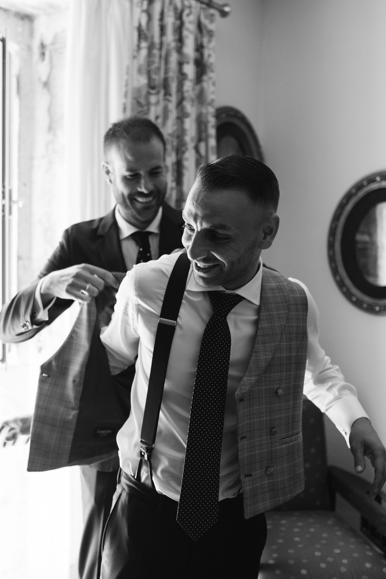 Groomsmen in black ties and formal attire laugh together while getting ready for a wedding celebration.