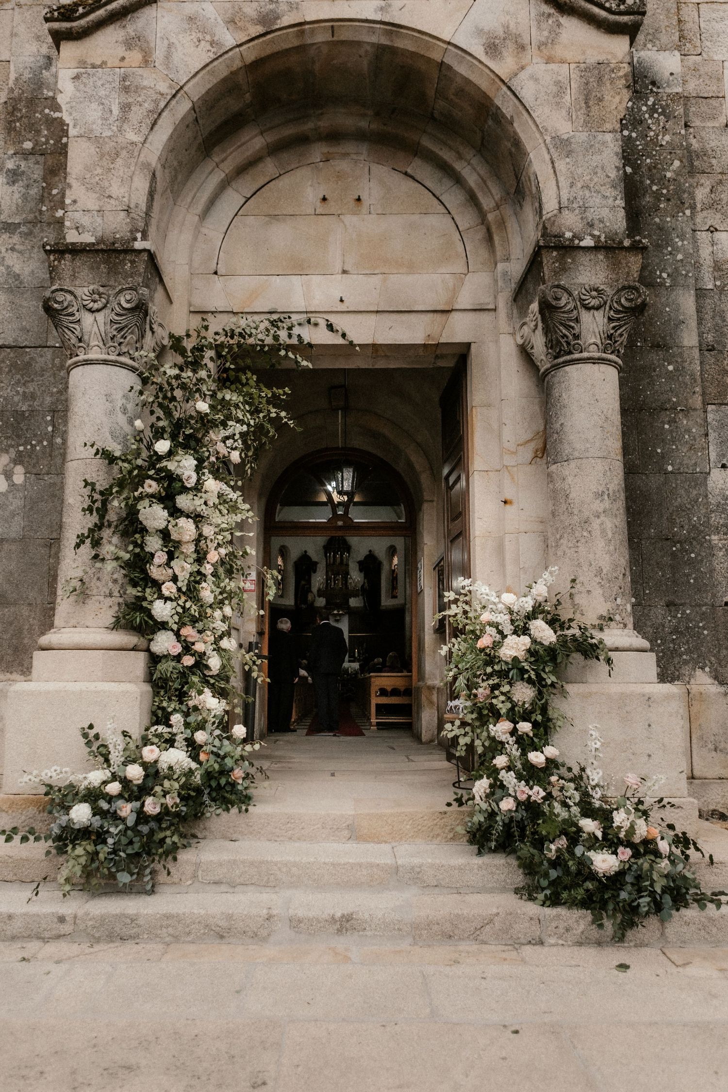 Beautiful stone church entrance archway decorated with elegant white floral arrangements for a wedding ceremony.