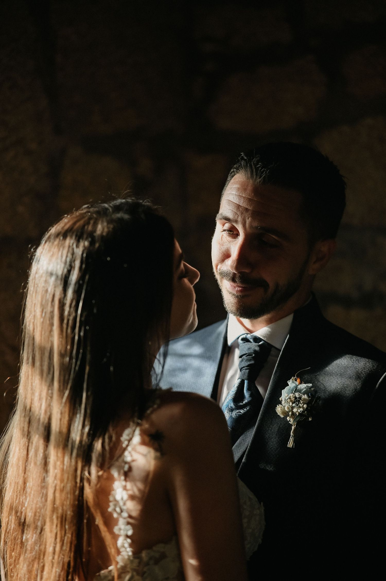 A romantic couple shares an intimate moment during their sunset wedding photoshoot in a dimly lit setting.