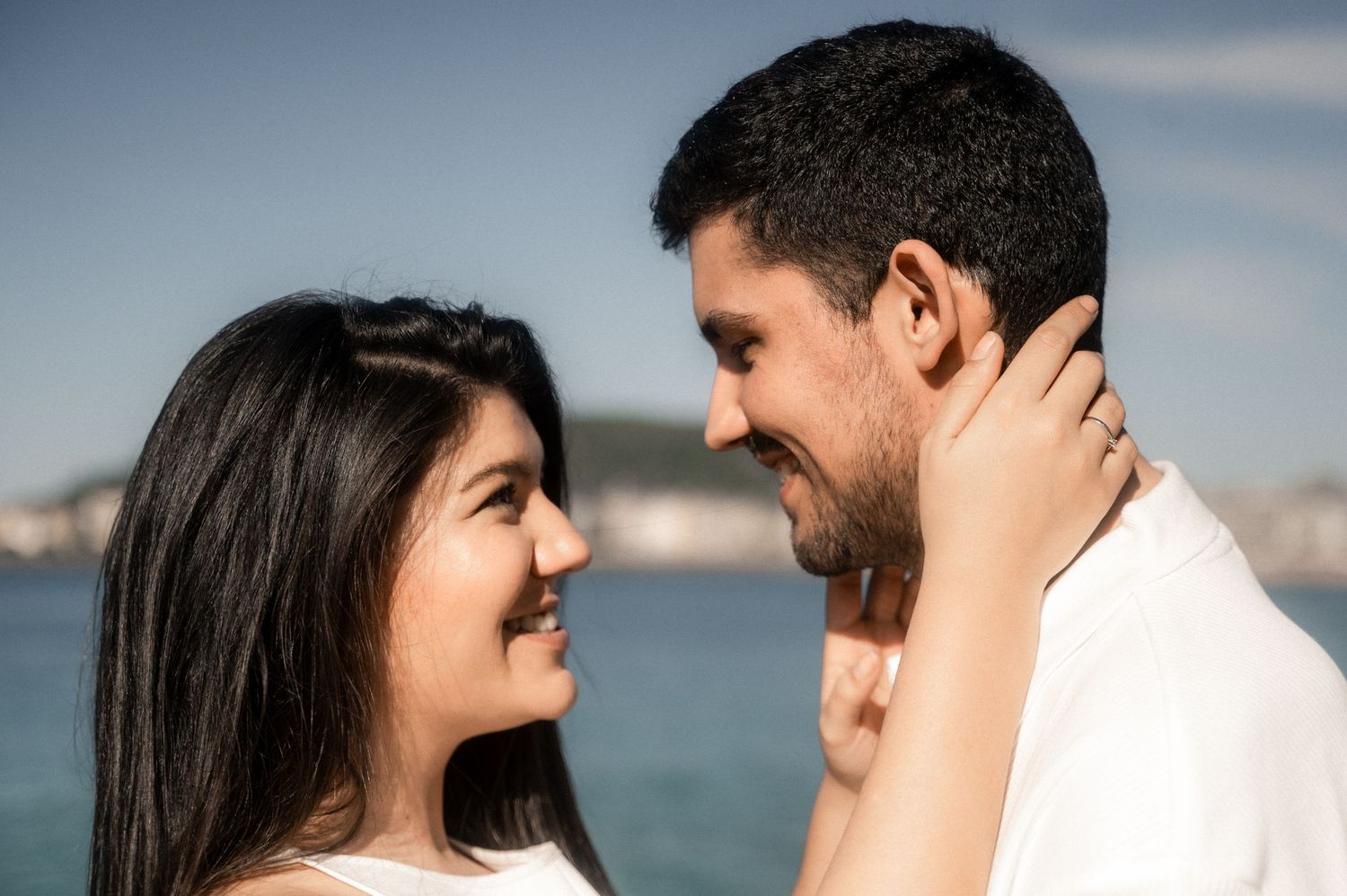A couple shares an intimate moment together against a blurred waterfront backdrop in warm sunlight.