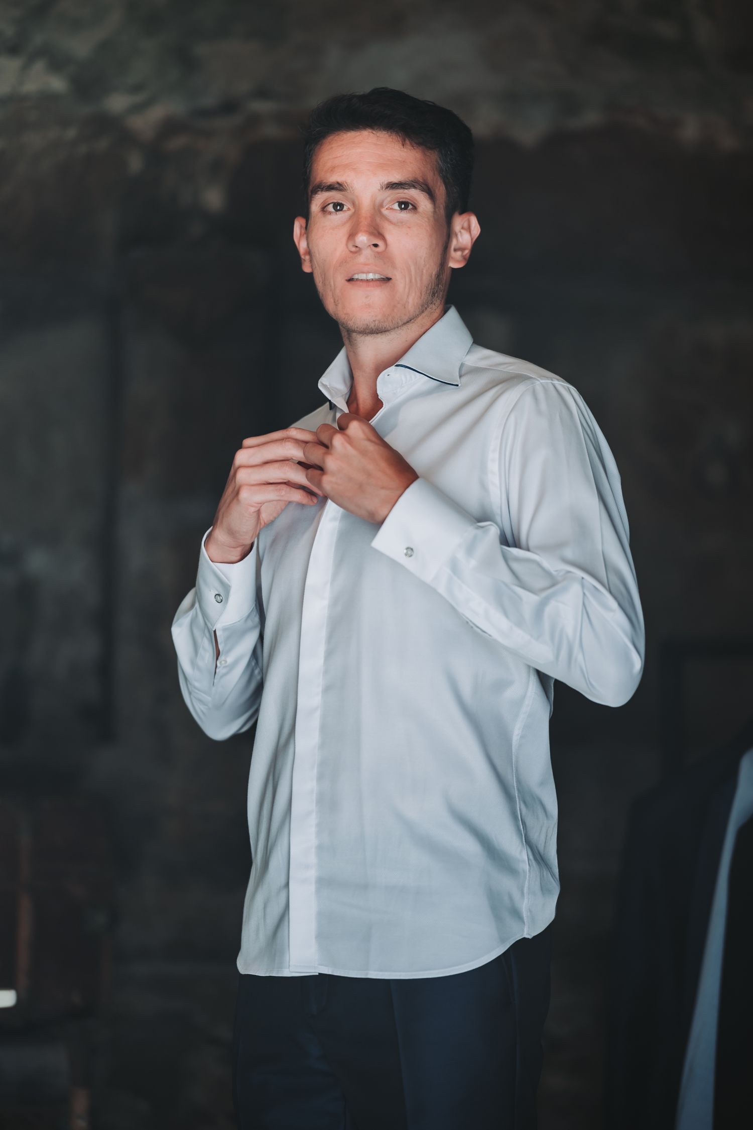 Person in white dress shirt adjusting collar and tie against dark background.