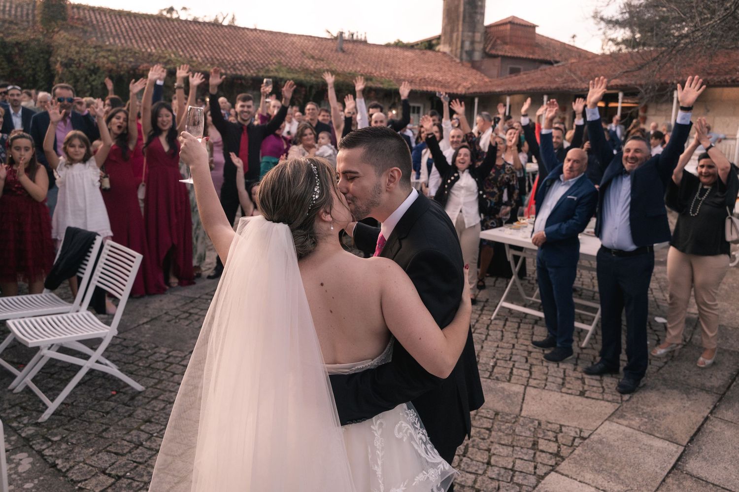 Wedding guests dance and celebrate on an outdoor stone patio during a festive reception party at sunset.