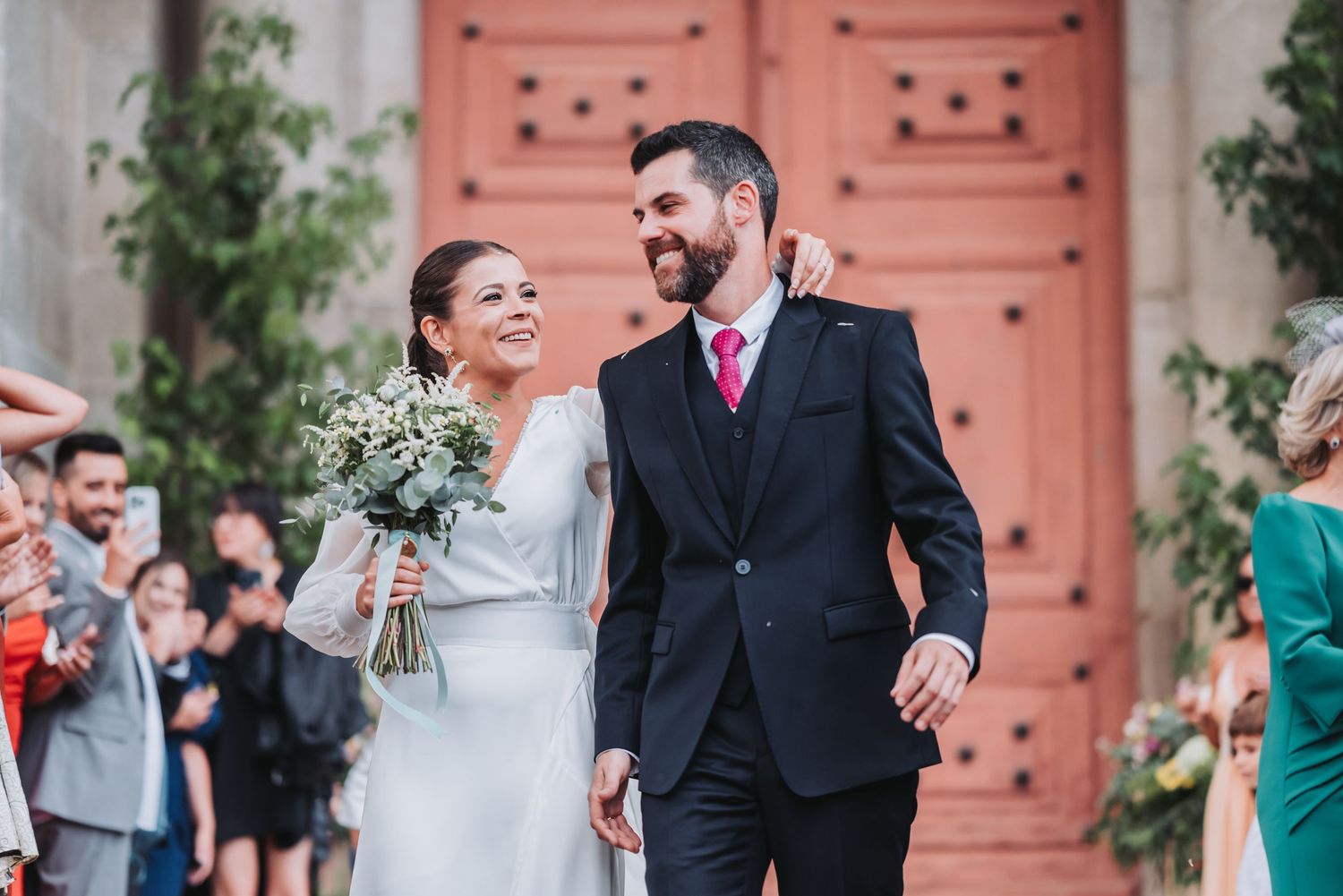 A joyful couple shares a romantic moment during their wedding ceremony in front of a coral-colored door.