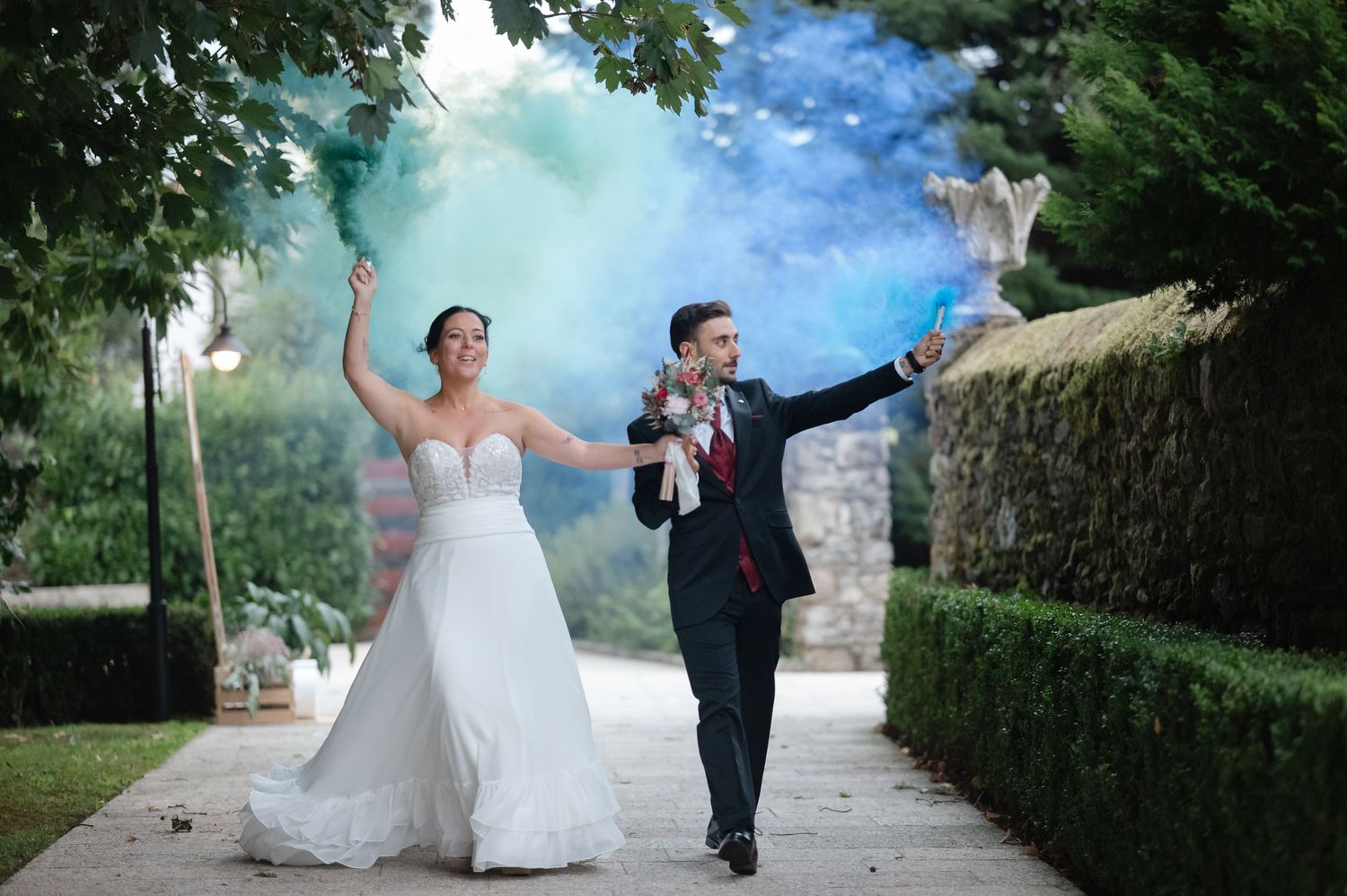 A couple celebrates joyfully on a garden path surrounded by lush greenery and dreamy blue atmosphere.