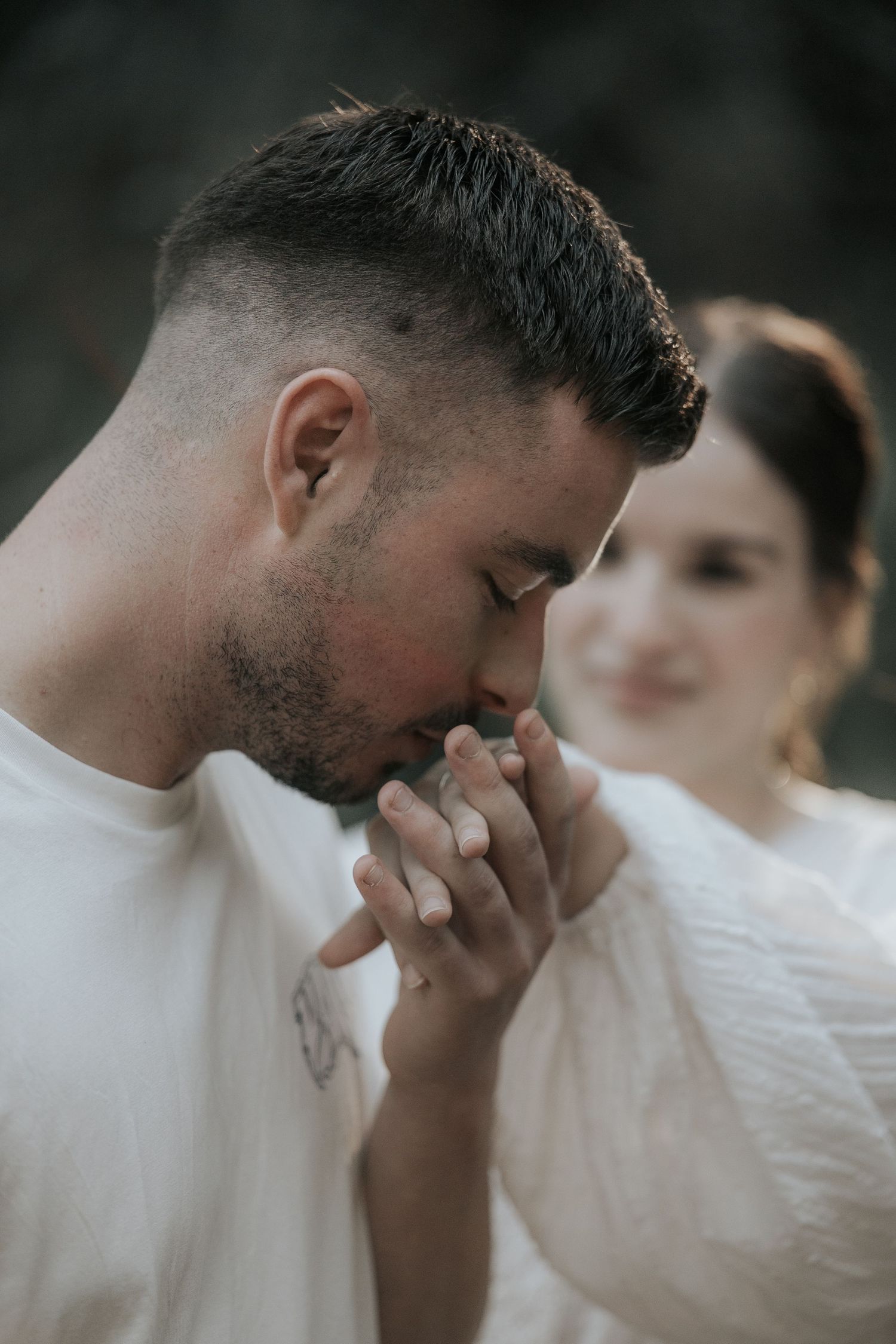 A tender moment captured in soft focus as a couple in white clothing share an intimate gesture outdoors.