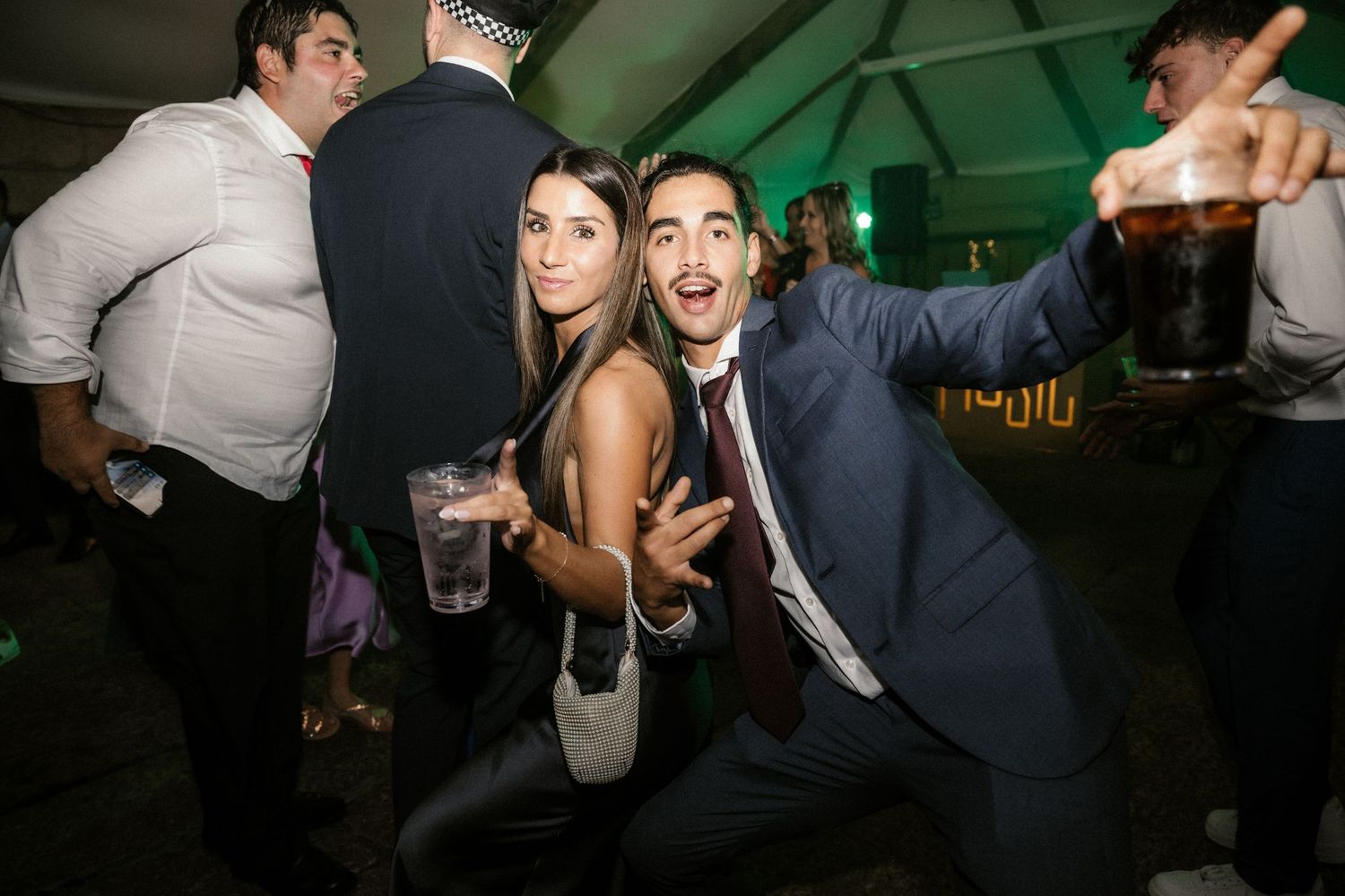 Party guests dancing and posing together at a nighttime celebration event with green lighting in the background.