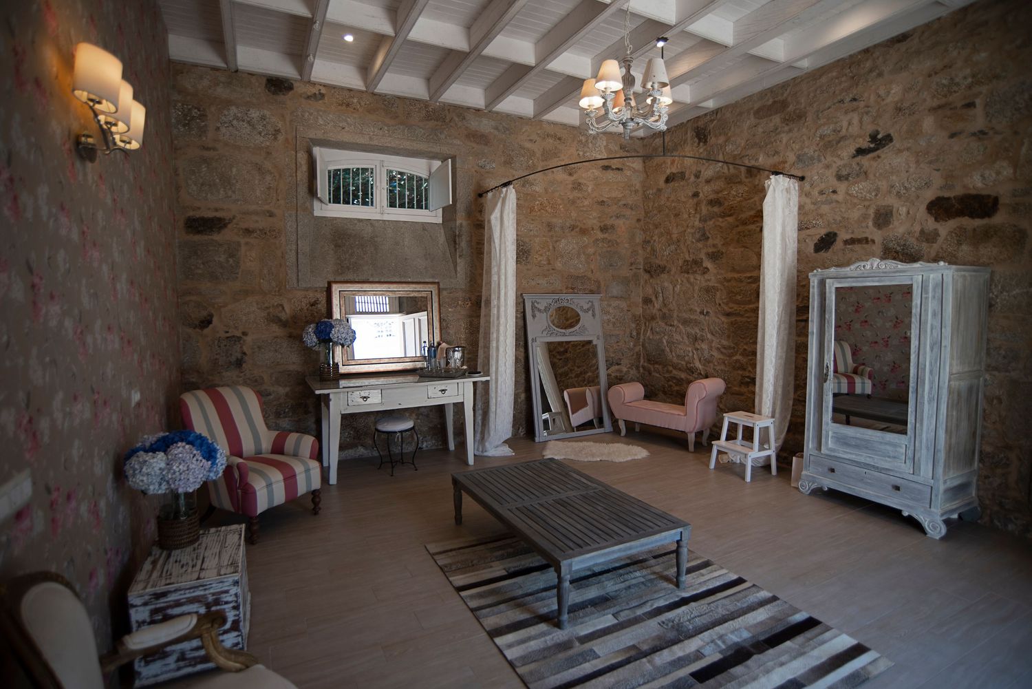 Interior view of a rustic stone-walled room with white ceiling beams and elegant chandelier lighting.