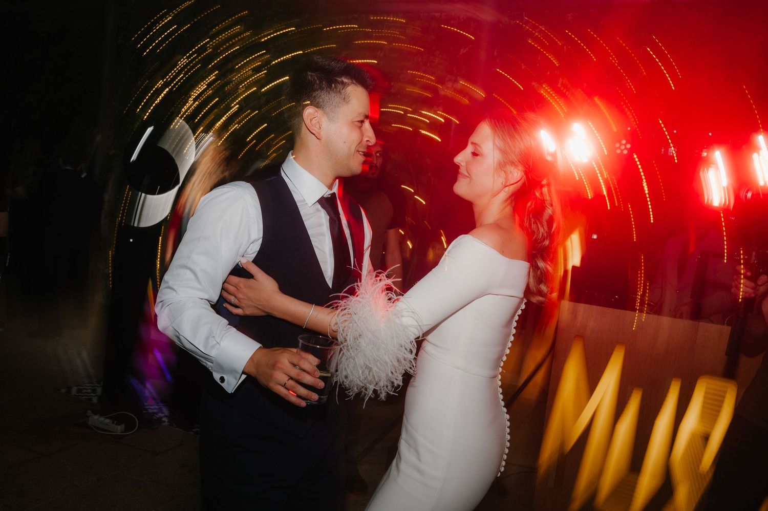 Dance floor filled with celebration under dramatic red lighting effects at evening wedding reception.
