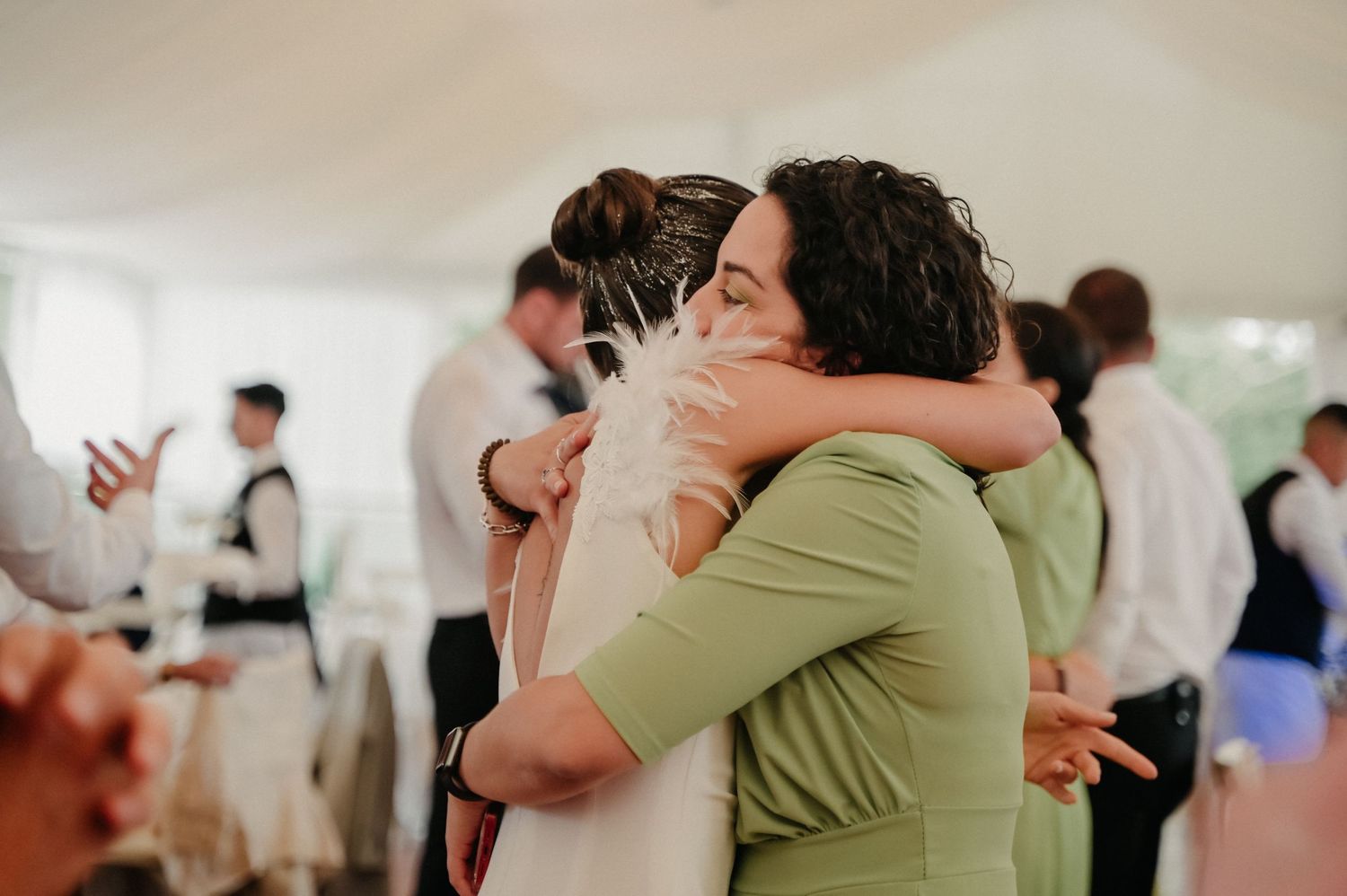 A series of emotional embraces and celebrations at a wedding reception in a bright indoor venue.