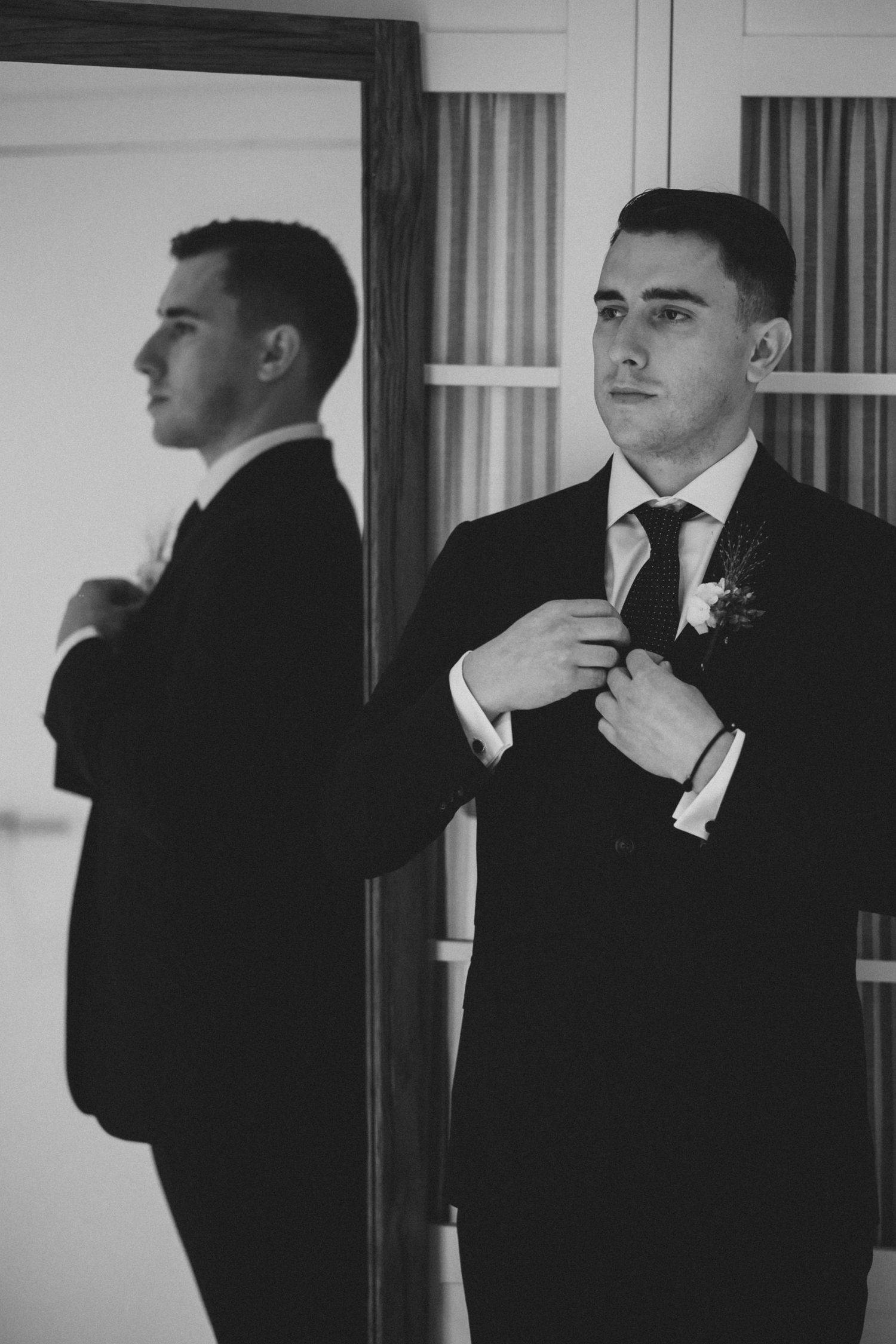 Black and white photo series showing a man in formal attire adjusting his tie and getting ready in front of a mirror.