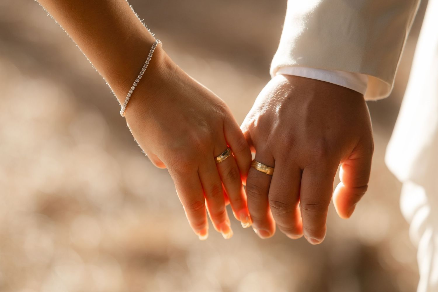 Hands of wedding couple exchanging rings during intimate ceremony with warm lighting.