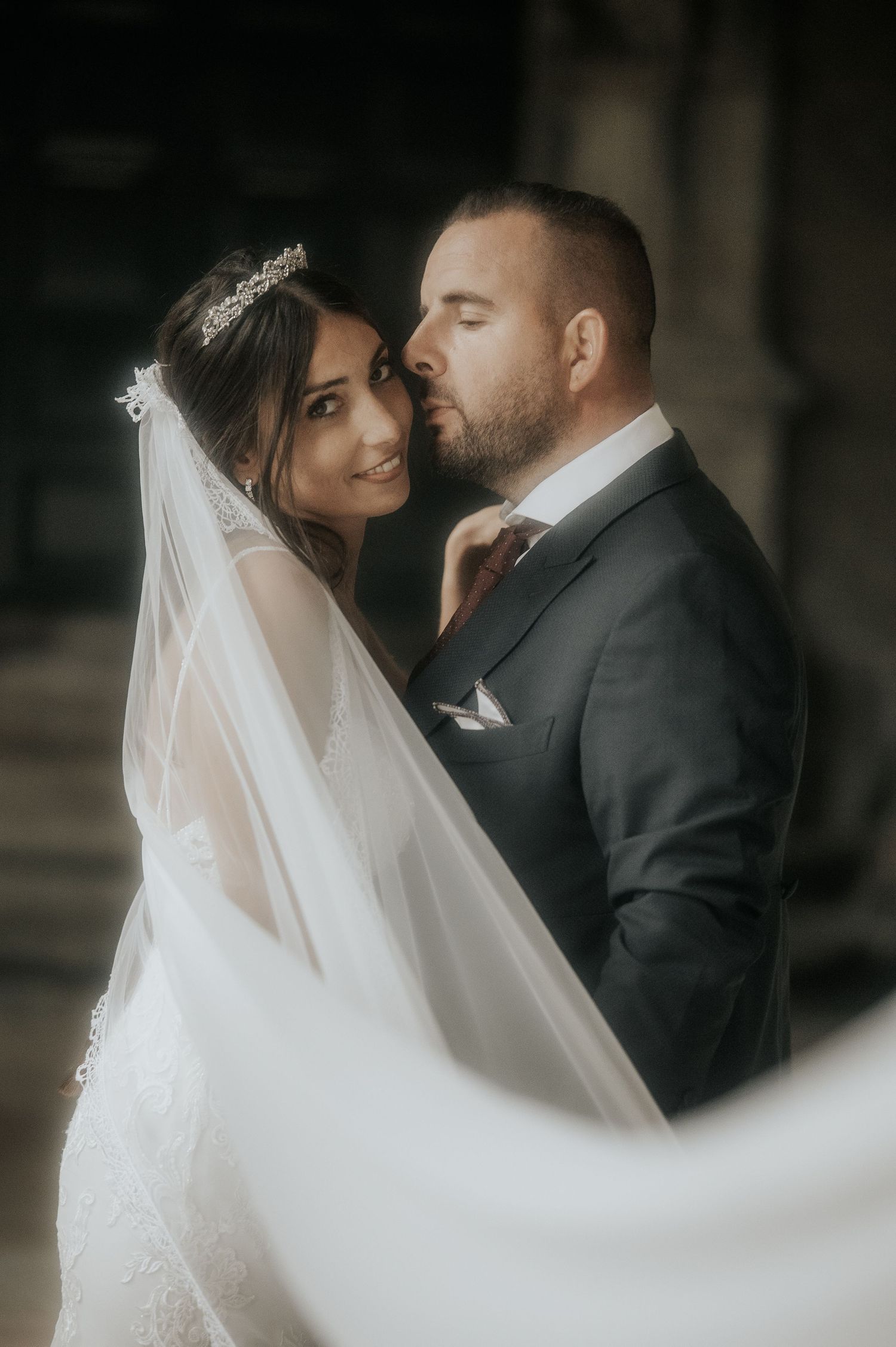 A romantic wedding portrait captures an intimate moment between newlyweds in soft, moody lighting.
