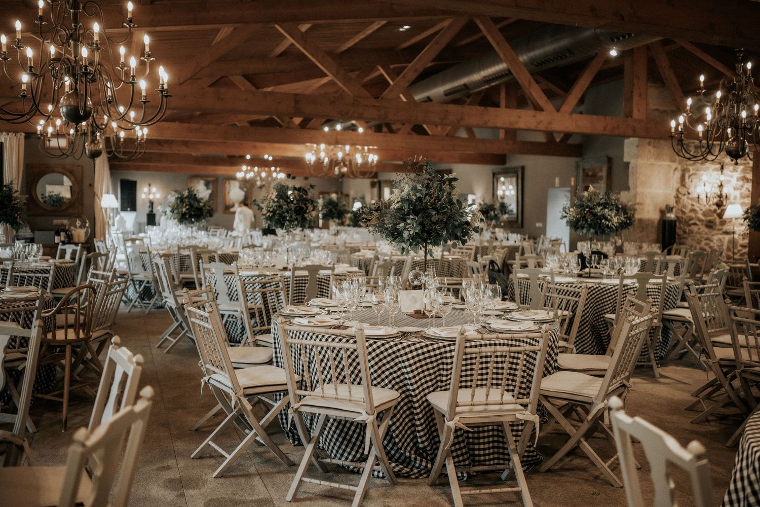 Elegant wedding reception venue with rustic wooden beams and crystal chandeliers set for dinner service.