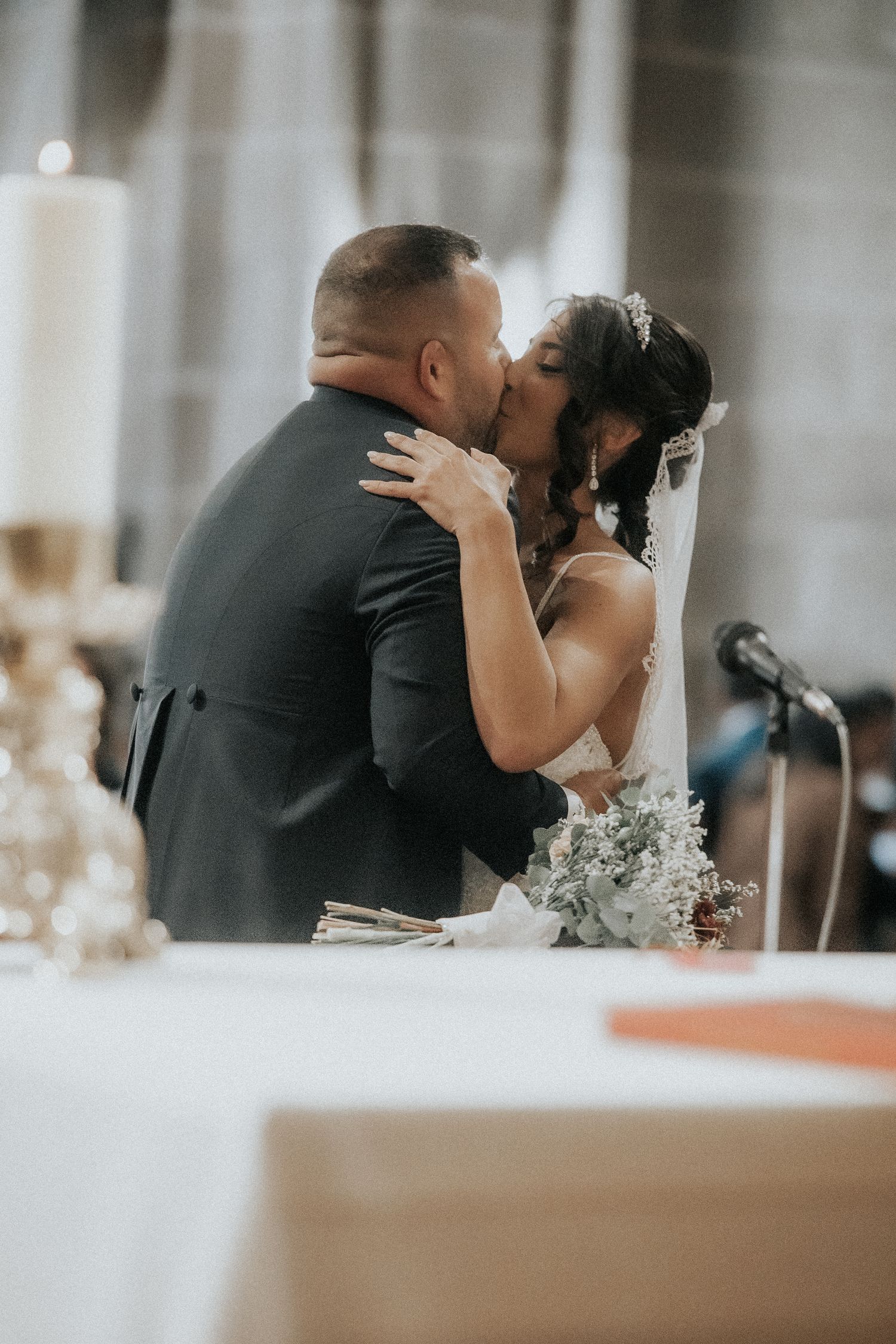 A romantic wedding couple shares a tender kiss at their reception with elegant table settings in the background.