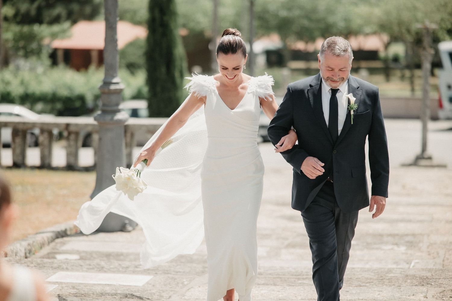 A couple walks together on a paved pathway surrounded by greenery on their wedding day.