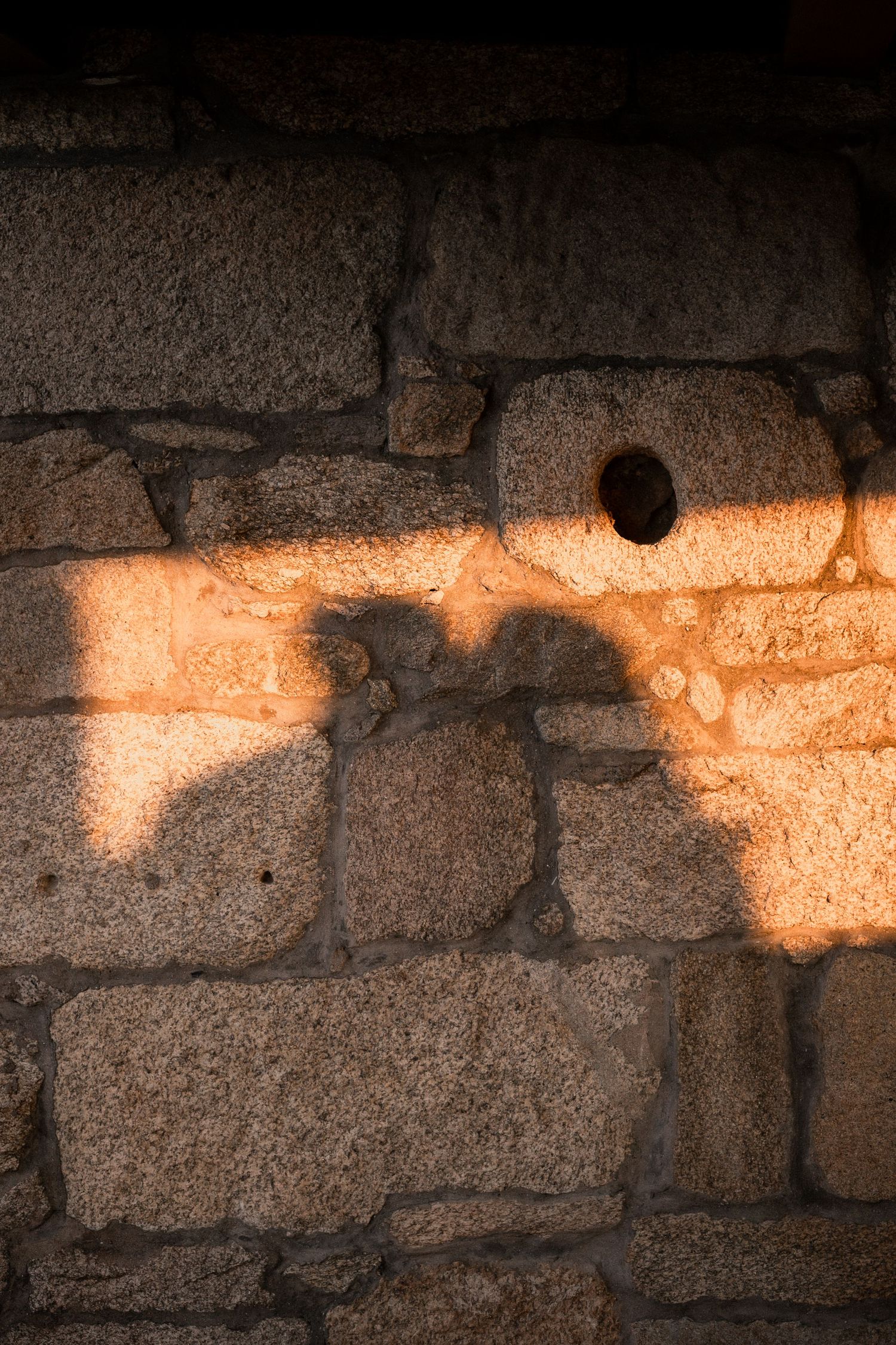 Sunlight creates a warm glow on a rustic stone wall with rough textured blocks.