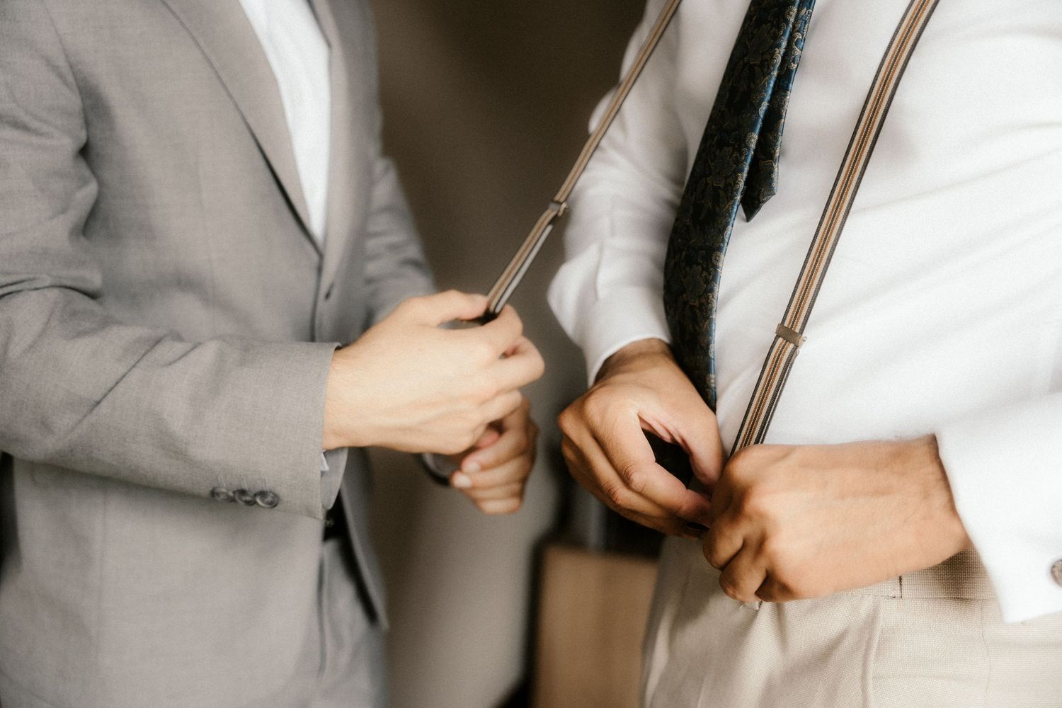 Close-up view of hands adjusting a white dress shirt sleeve and cuff button in natural lighting.