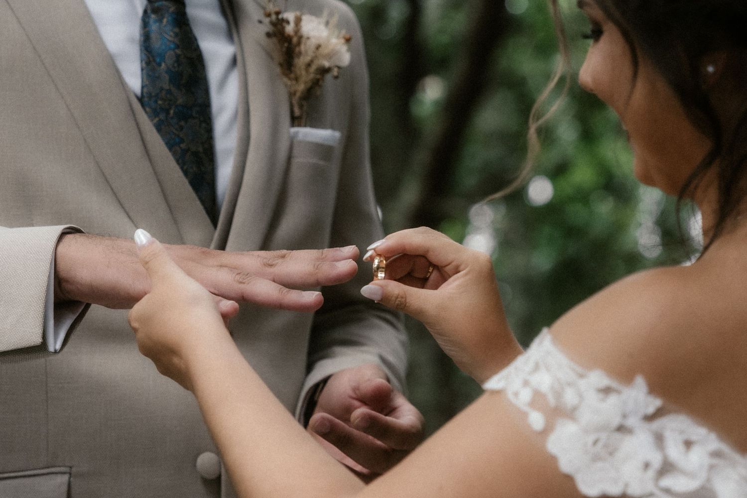 Intimate outdoor wedding ceremony with rings being exchanged under natural forest canopy.