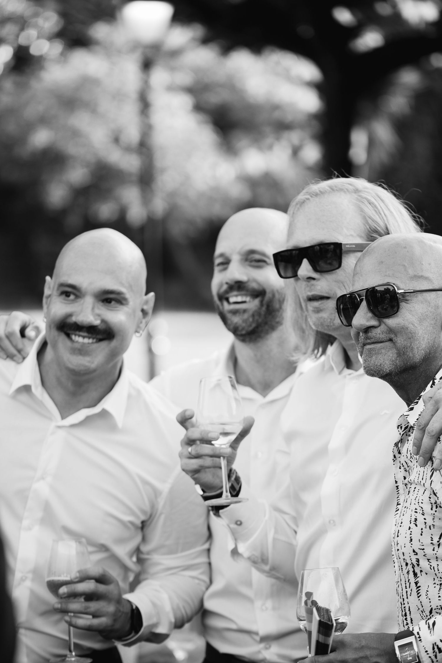 A black and white photo of men in white shirts laughing and holding drinks at an outdoor gathering.