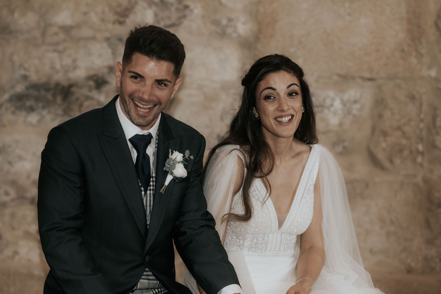 A happy couple poses for wedding photos in an elegant stone archway setting.