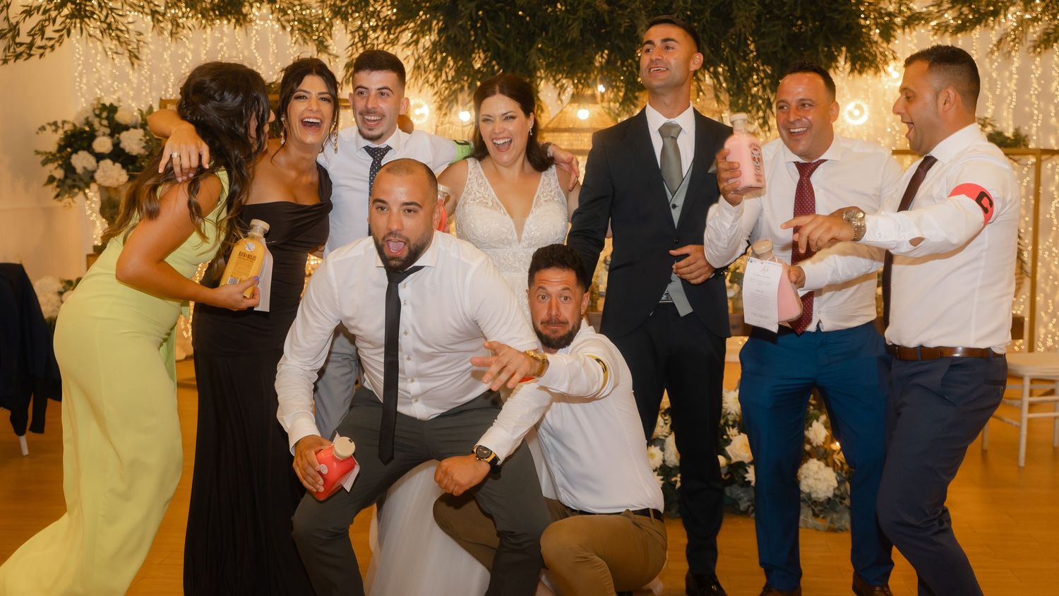 Wedding party dances together on wooden dance floor during evening reception celebration.
