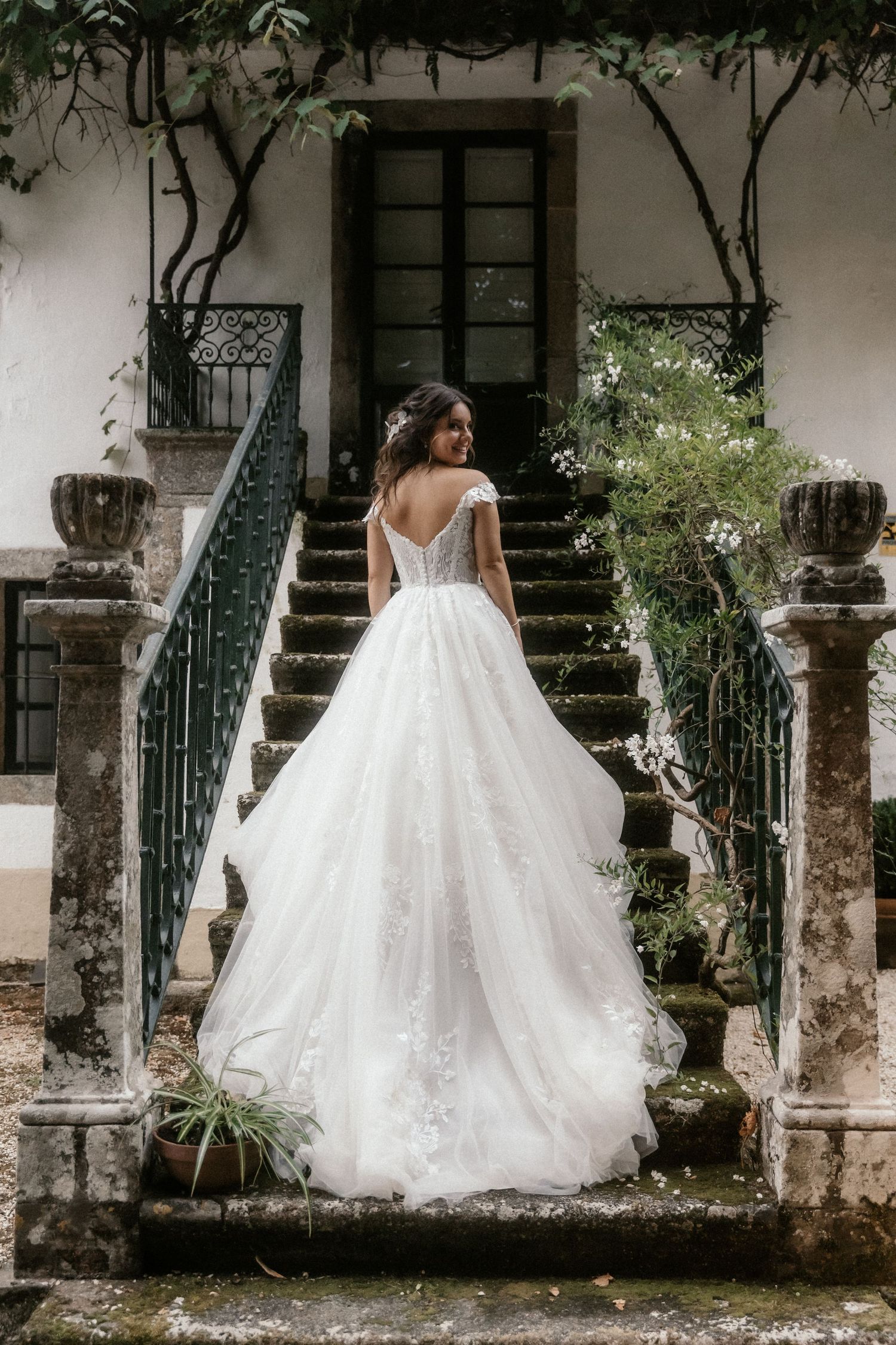 A bride in a flowing white wedding gown twirls gracefully on a stone patio with vintage architectural elements.