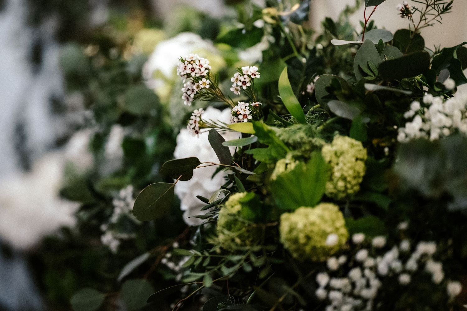 White and green floral arrangement with hydrangeas and delicate blooms against a blurred background.