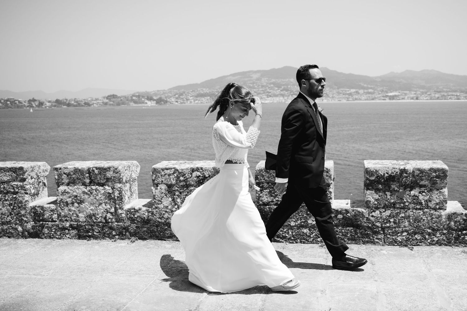 A black and white wedding photo series shows a couple in formal attire against a scenic coastal backdrop.