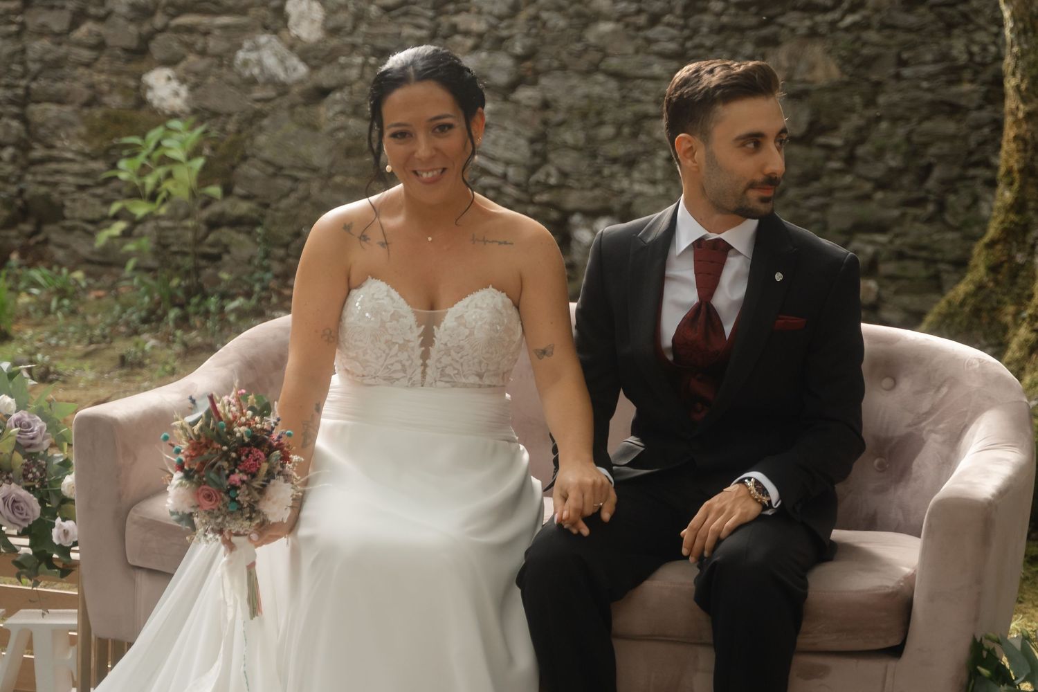 Elegant wedding celebration with guests seated on plush furniture against a stone wall backdrop.