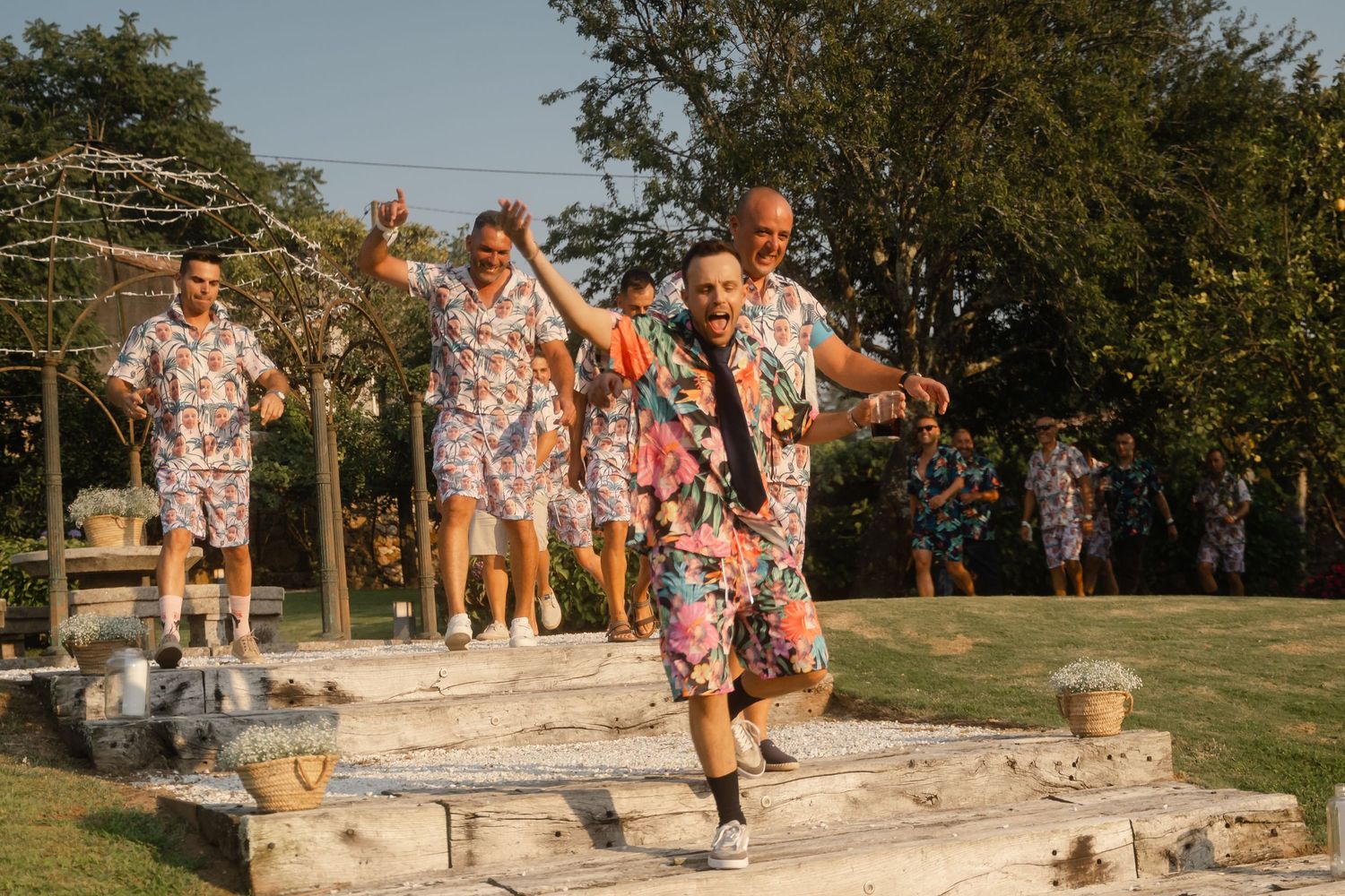 Group of people in matching floral outfits dancing and celebrating outdoors on a sunny day.